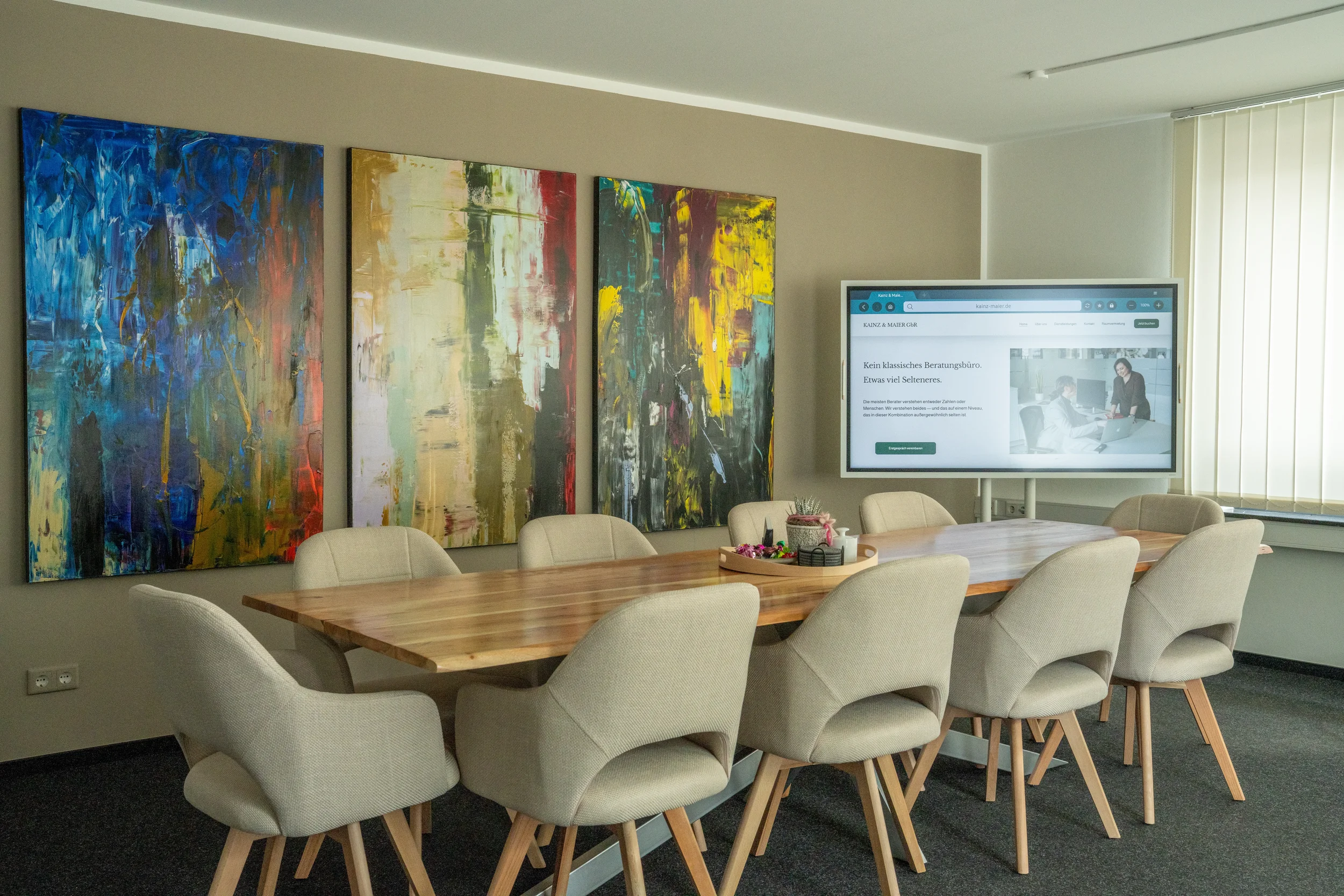 Heller Tagungsraum in Münster mit modernem Holz-Konferenztisch, Polsterstühlen und großem Präsentationsbildschirm. Perfekt für Workshops und Seminare in professioneller Atmosphäre.