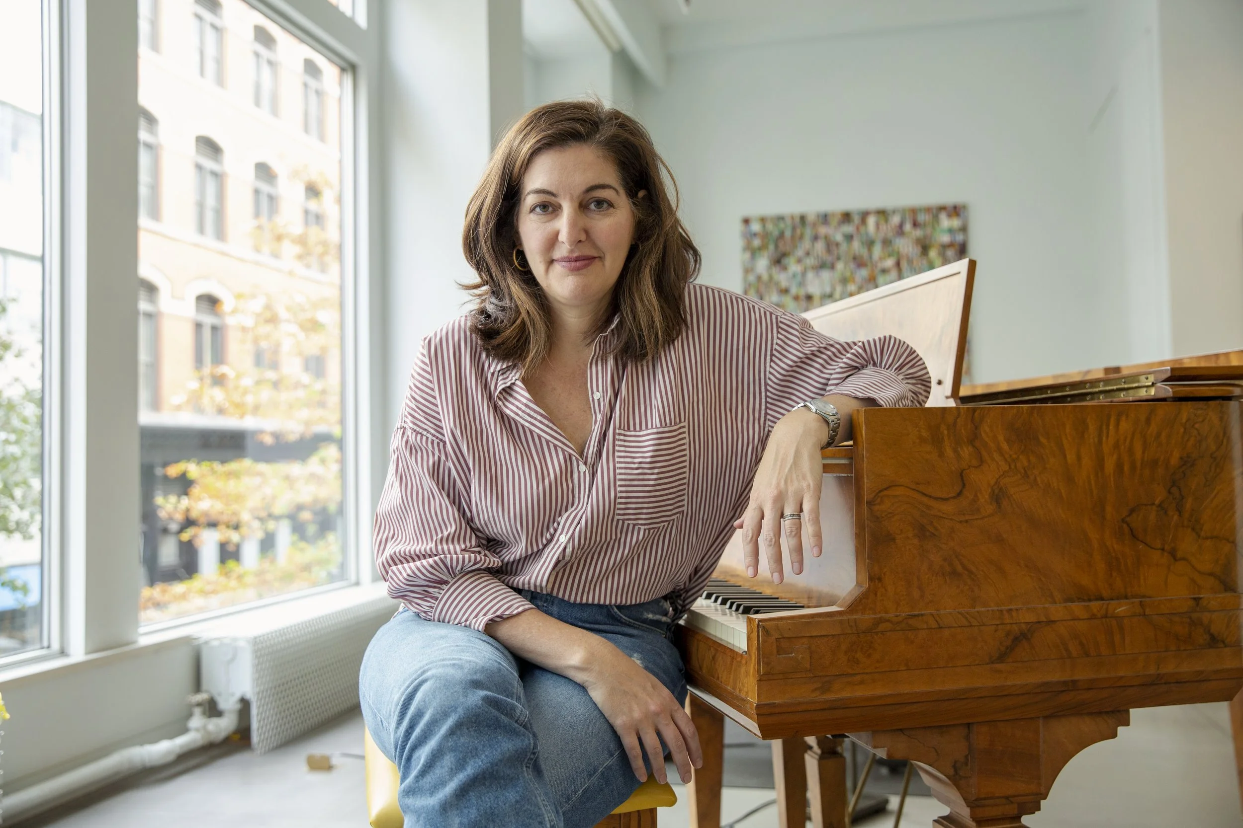 Rachel Schneider poses for a portrait, sitting on her piano, taken for Business Insider.