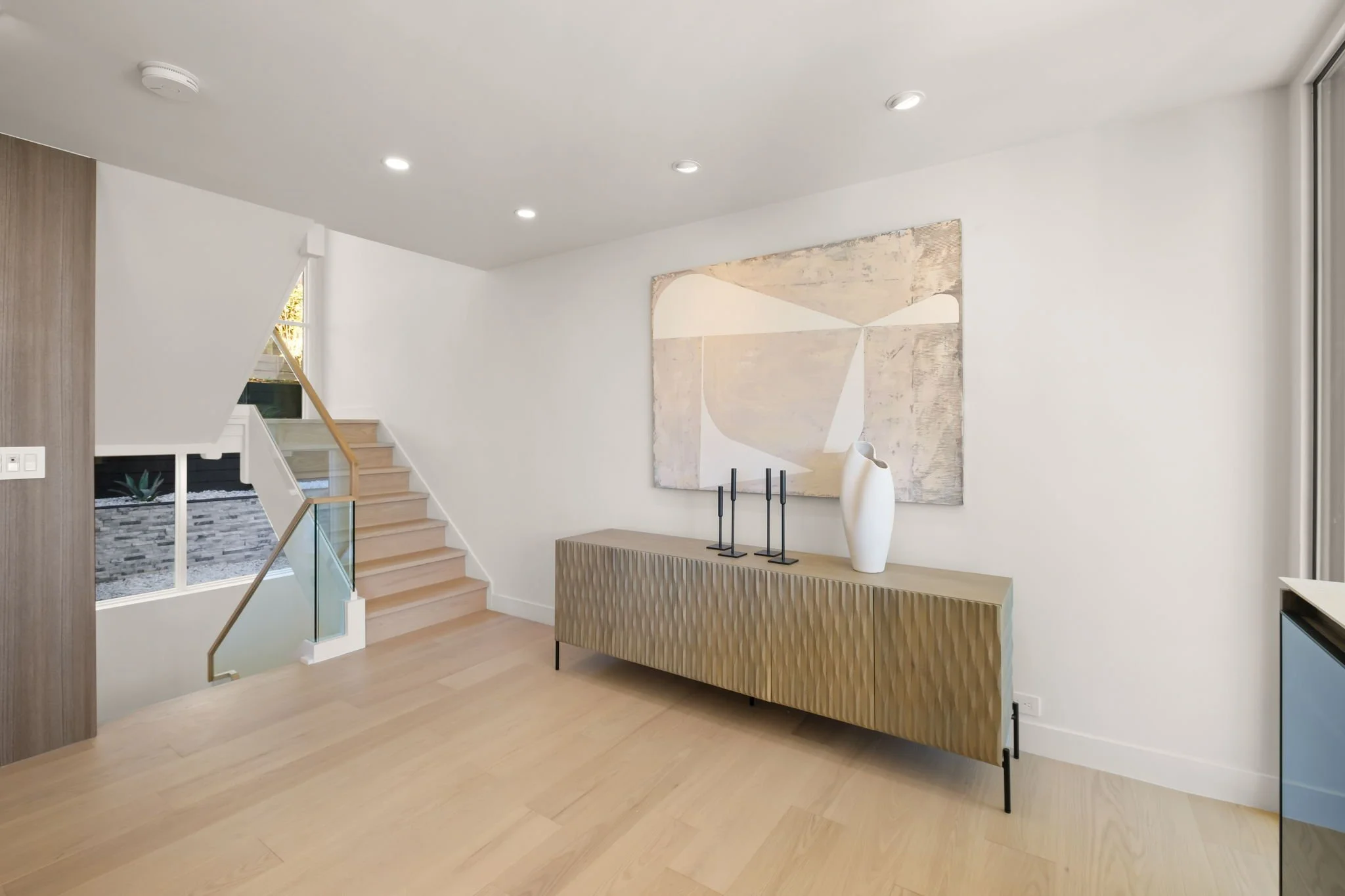 Modern interior hallway with staircase, minimalist decor, abstract artwork, beige sideboard, and decorative vases.