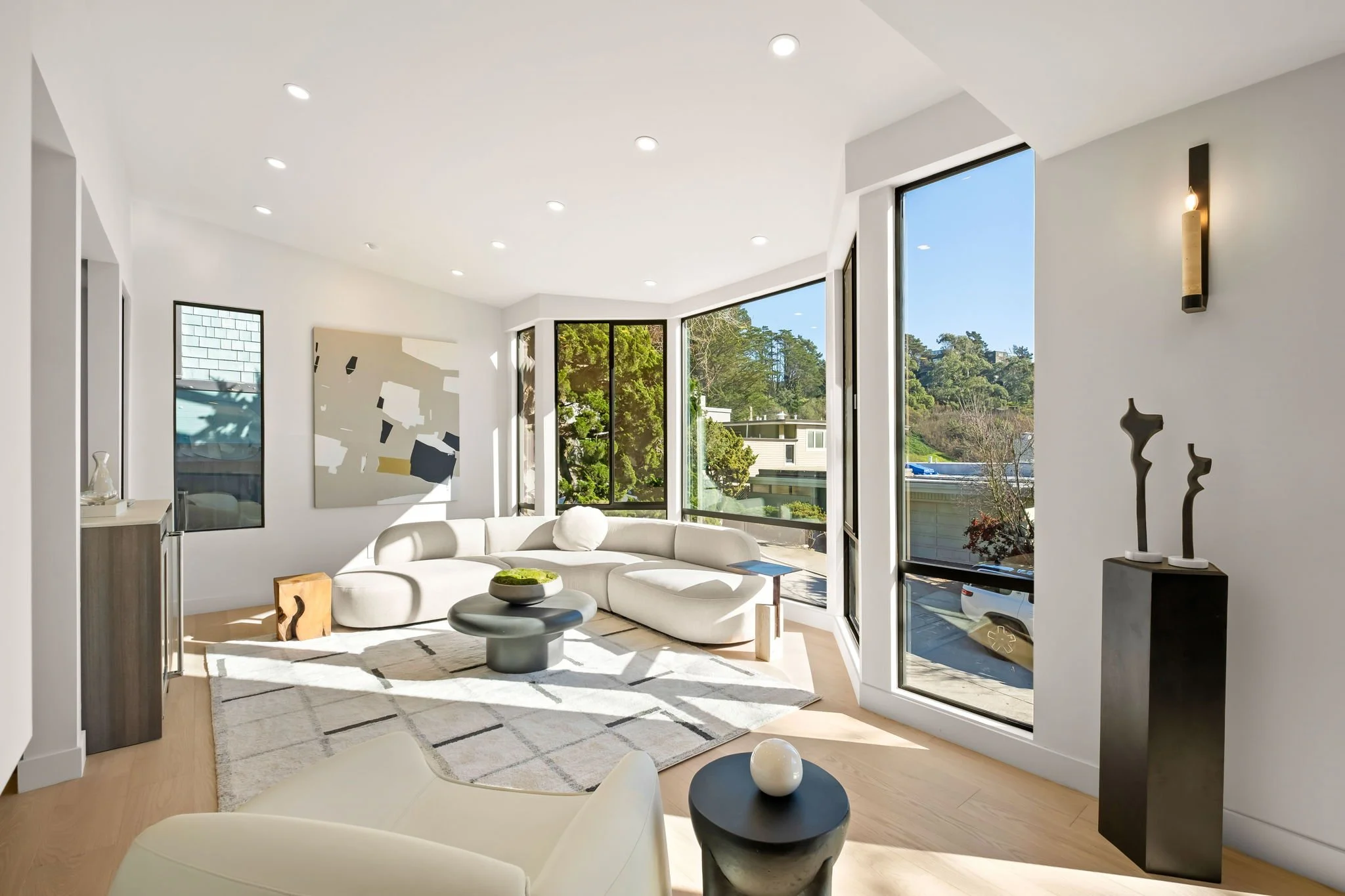 Bright living room with large windows, white sectional sofa, abstract artwork, and modern decor