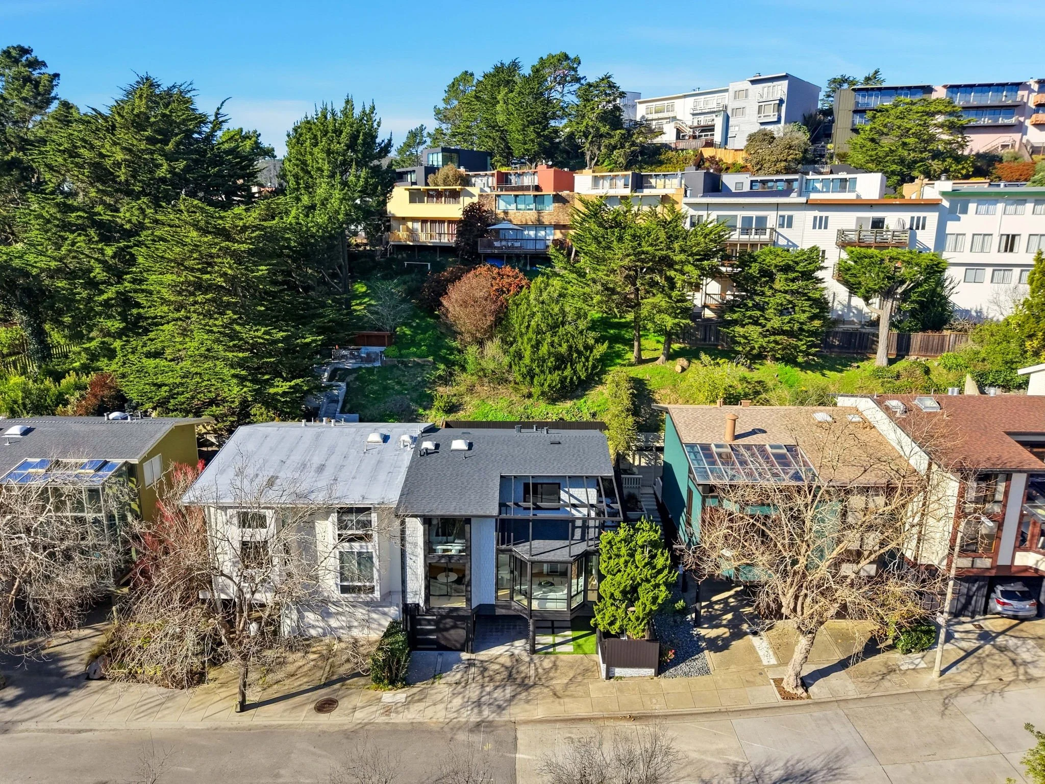 Aerial view of a residential area with modern houses and lush green trees on a sunny day.