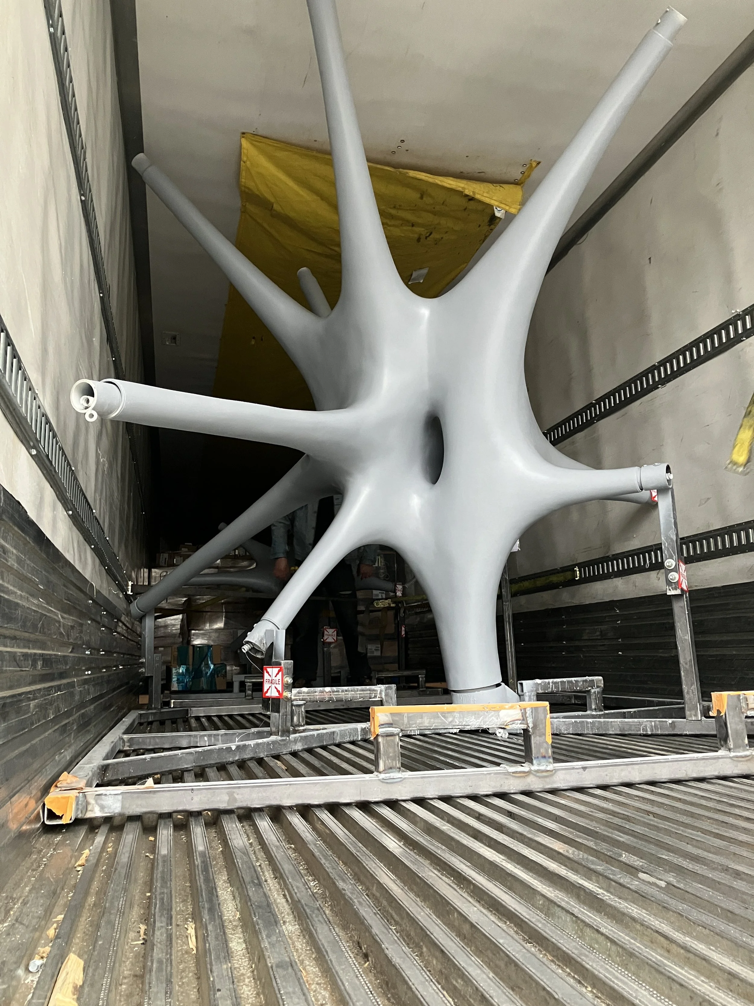 An art installation or sculpture resembling a starfish, light gray in color, with multiple elongated arms, secured on a platform inside a truck or storage container.