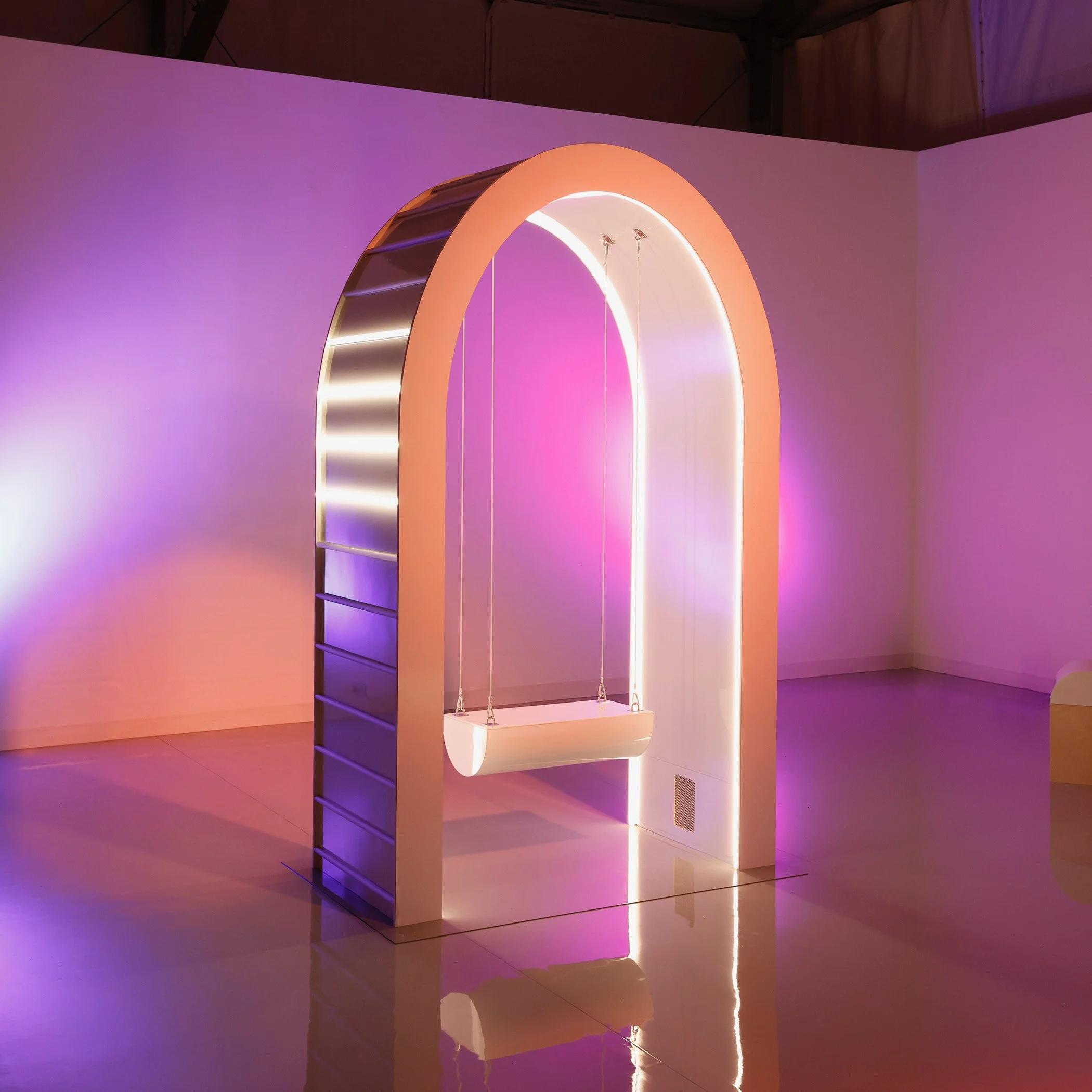 Modern art installation featuring a white arched frame with integrated LED lighting and a suspended white swing in a gallery with pink and purple ambient lighting.