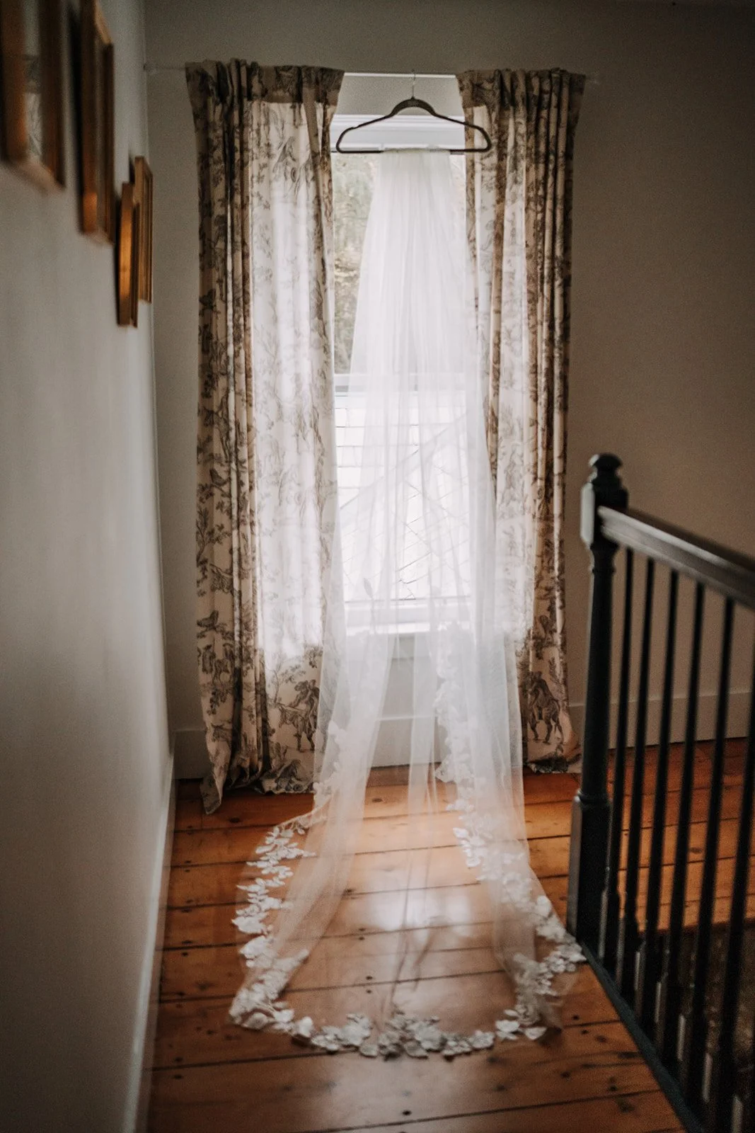 A sheer white curtain with floral embroidery hanging in front of a window, with floral-patterned drapes on either side.