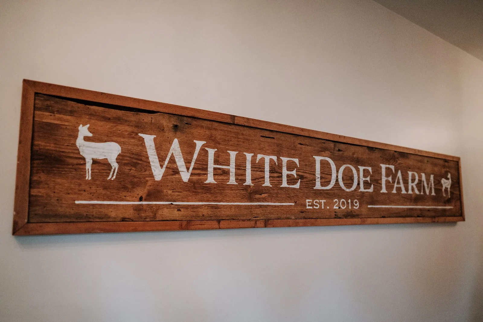 Wooden farm sign for White Doe Farm, established in 2019, with silhouettes of a dog and a goat.