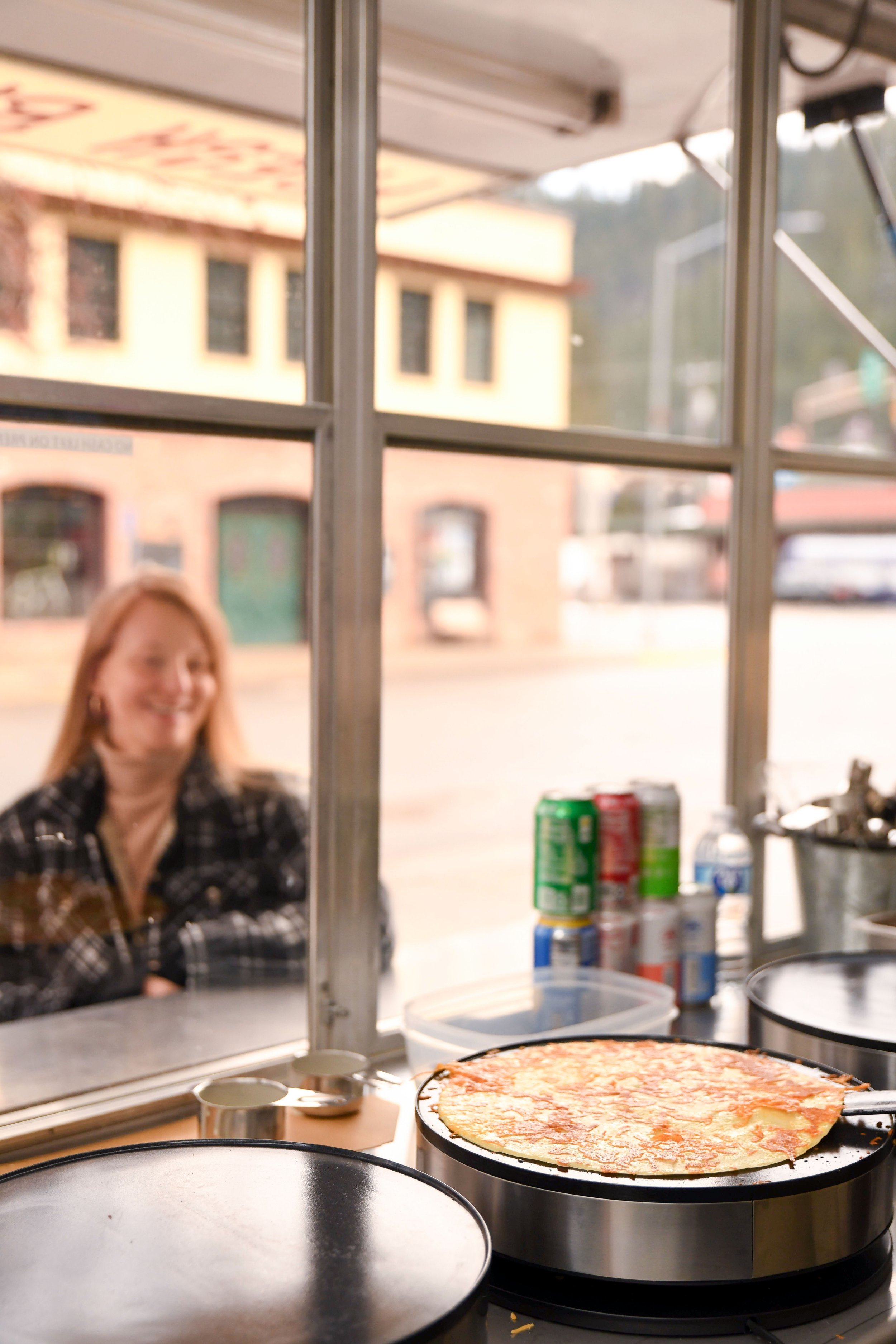 A sliced cheese pizza cooking on an electric griddle, with a person smiling outside the window in the background.