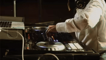 Queer DJ in white dress shirt mixing music behing a DJ console at a wedding in a dimly lit setting in Tulum, Quintana Roo, Mexico.