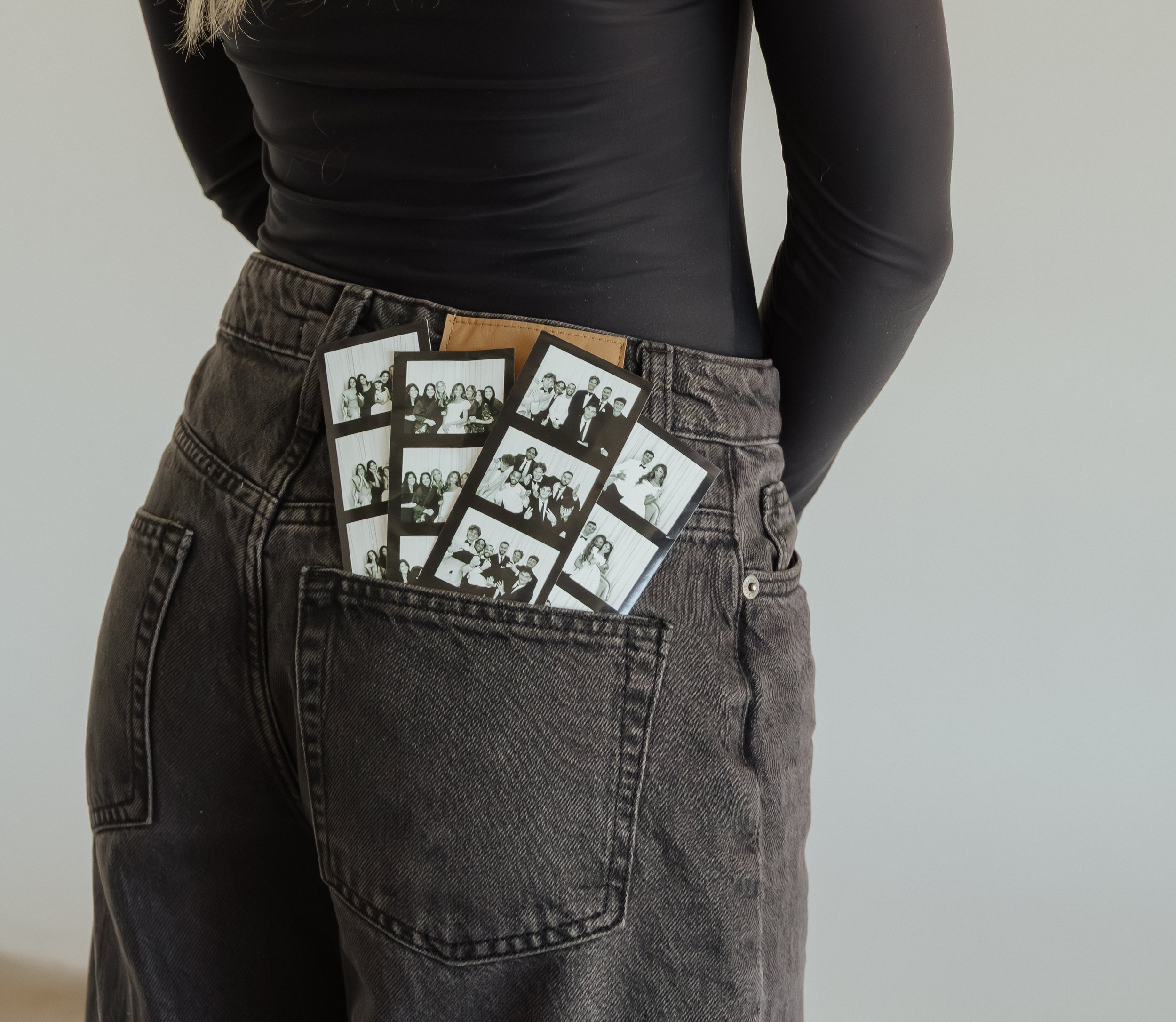 Person wearing black top and gray jeans with photo booth strips in back pocket.