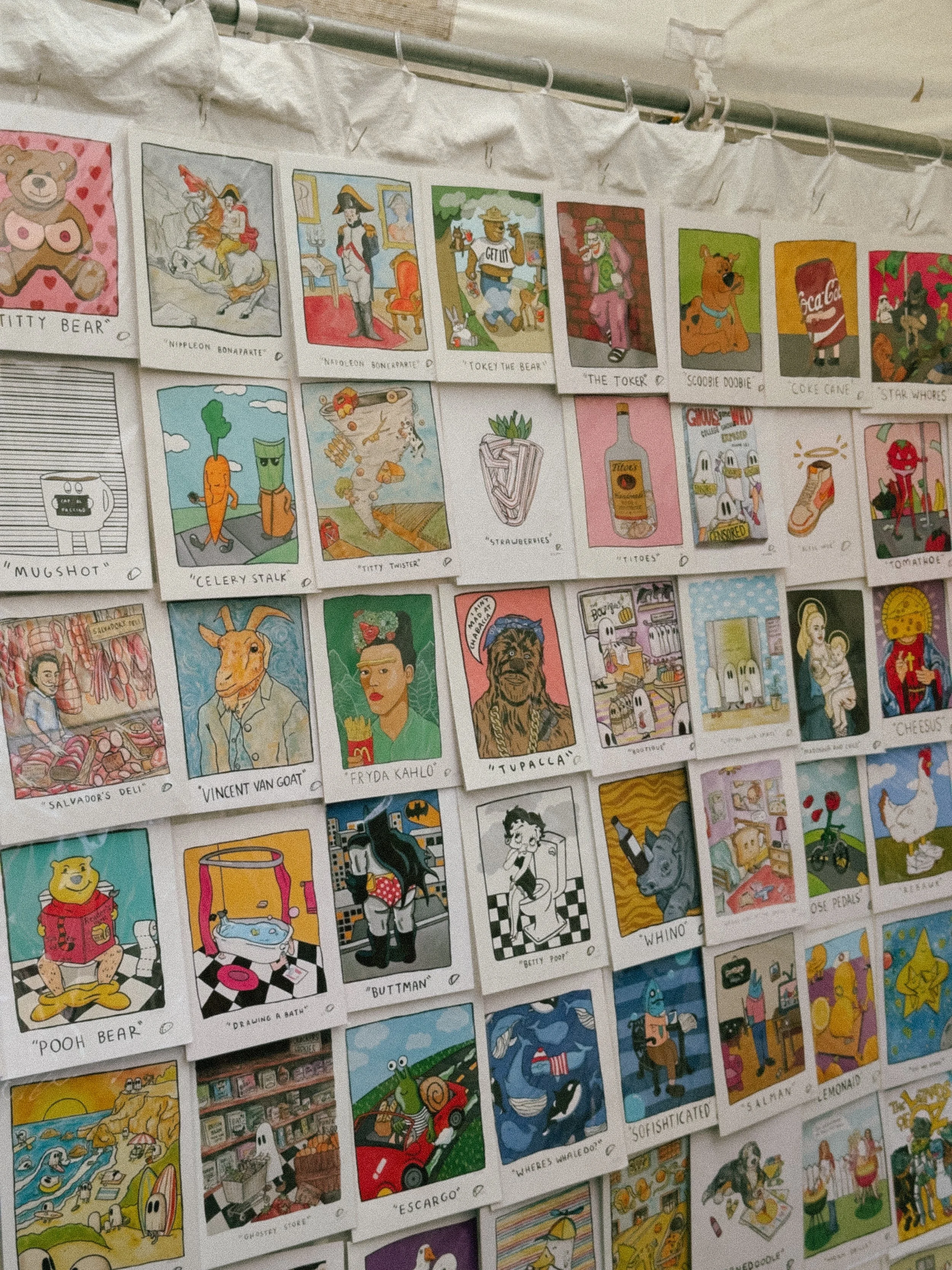 Wall display of colorful illustrated cards featuring various characters and names such as 'Nitty Bear,' 'Nippleon Bonaparte,' 'Tokei The Bear,' 'Vincent Van Goat,' and 'Pooh Bear.'