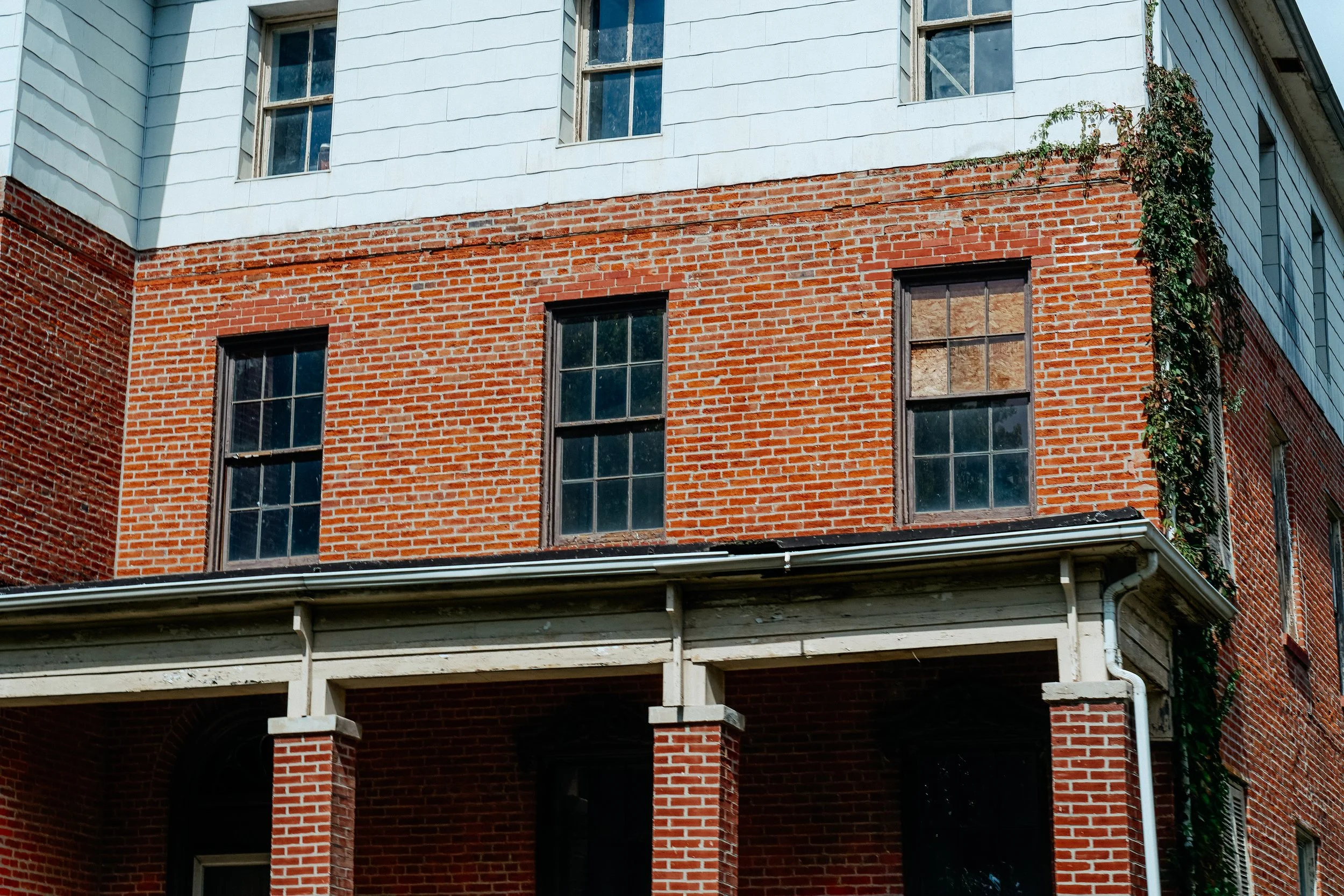 Close-up of a brick building with three windows and white wood siding at the top.