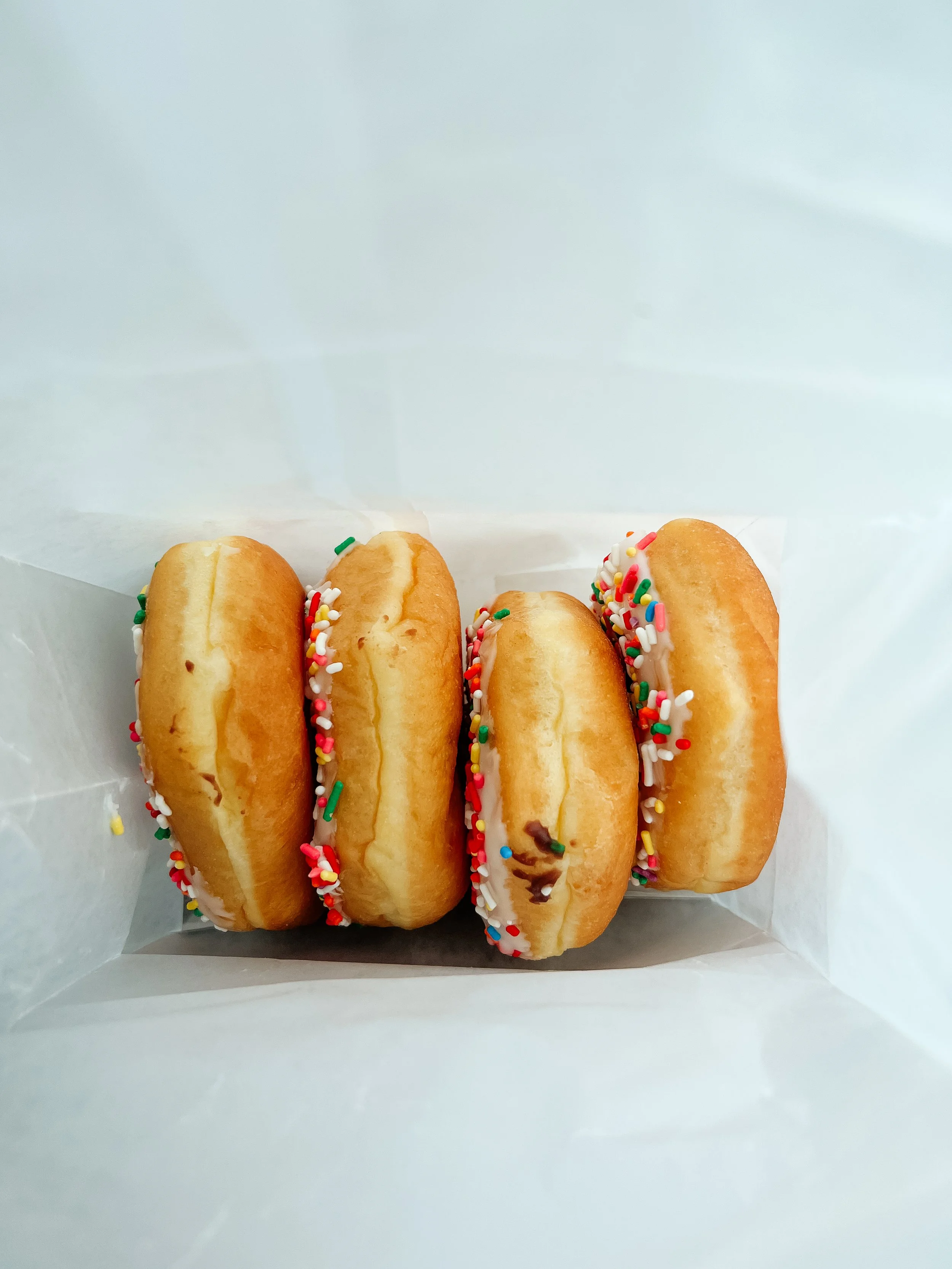 Four mini donuts with colorful sprinkles in a white paper bag.