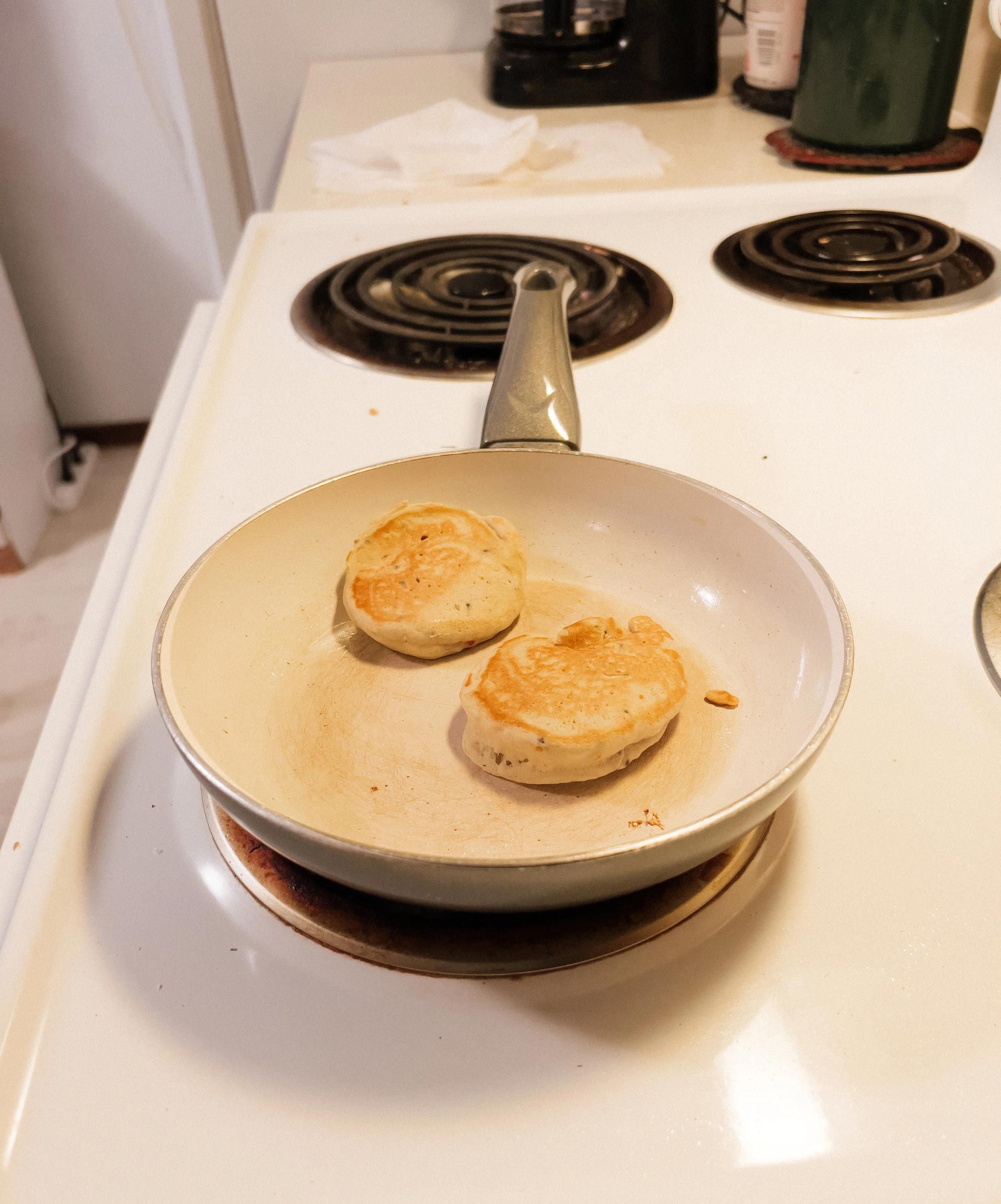 Two breakfast biscuits in a white frying pan on an electric stovetop in a kitchen.