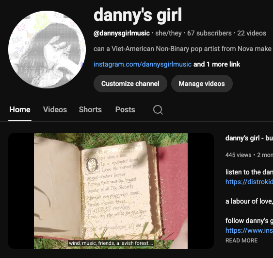 Screenshot of a YouTube channel titled "danny's girl" with a profile picture of a person singing or speaking into a microphone. The channel has 67 subscribers and features videos related to music by a non-binary pop artist. The video preview shows an open book lying on grass with sunflowers nearby, and captions reading "wind, music, friends, a lavish forest."