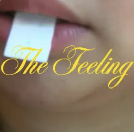 Close-up of a person biting a white paper strip, with the words "The Feeling" written in yellow cursive font over the image.