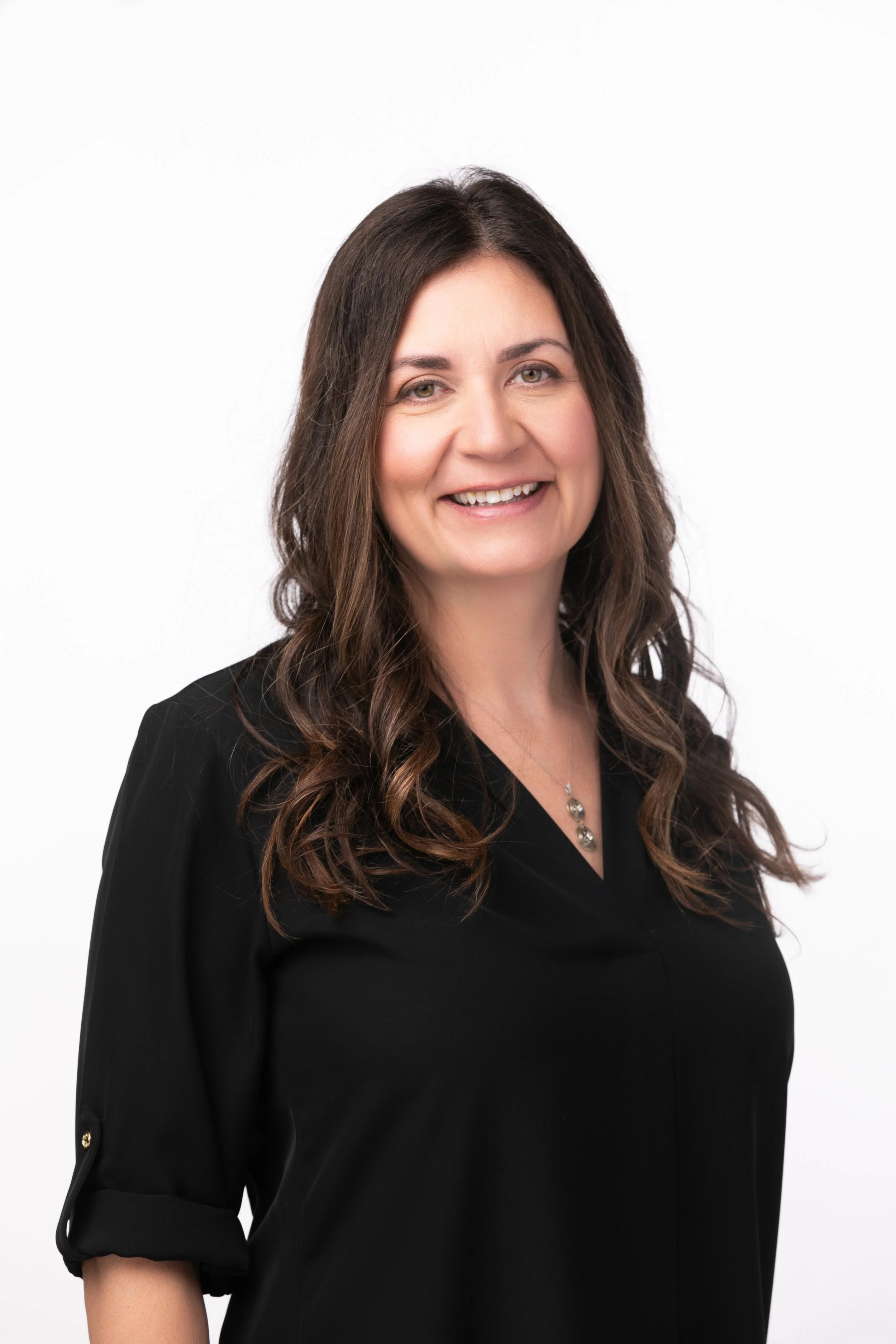 A woman with long brown hair smiling, wearing a black top with rolled sleeves and a necklace, against a white background.