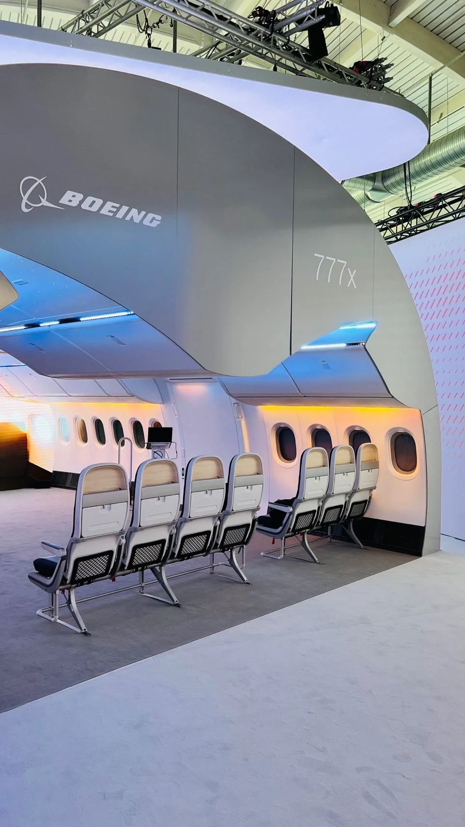 AIX tradeshow booth showcasing a Boeing 777X airplane cabin section with seats, illuminated with colorful lighting.