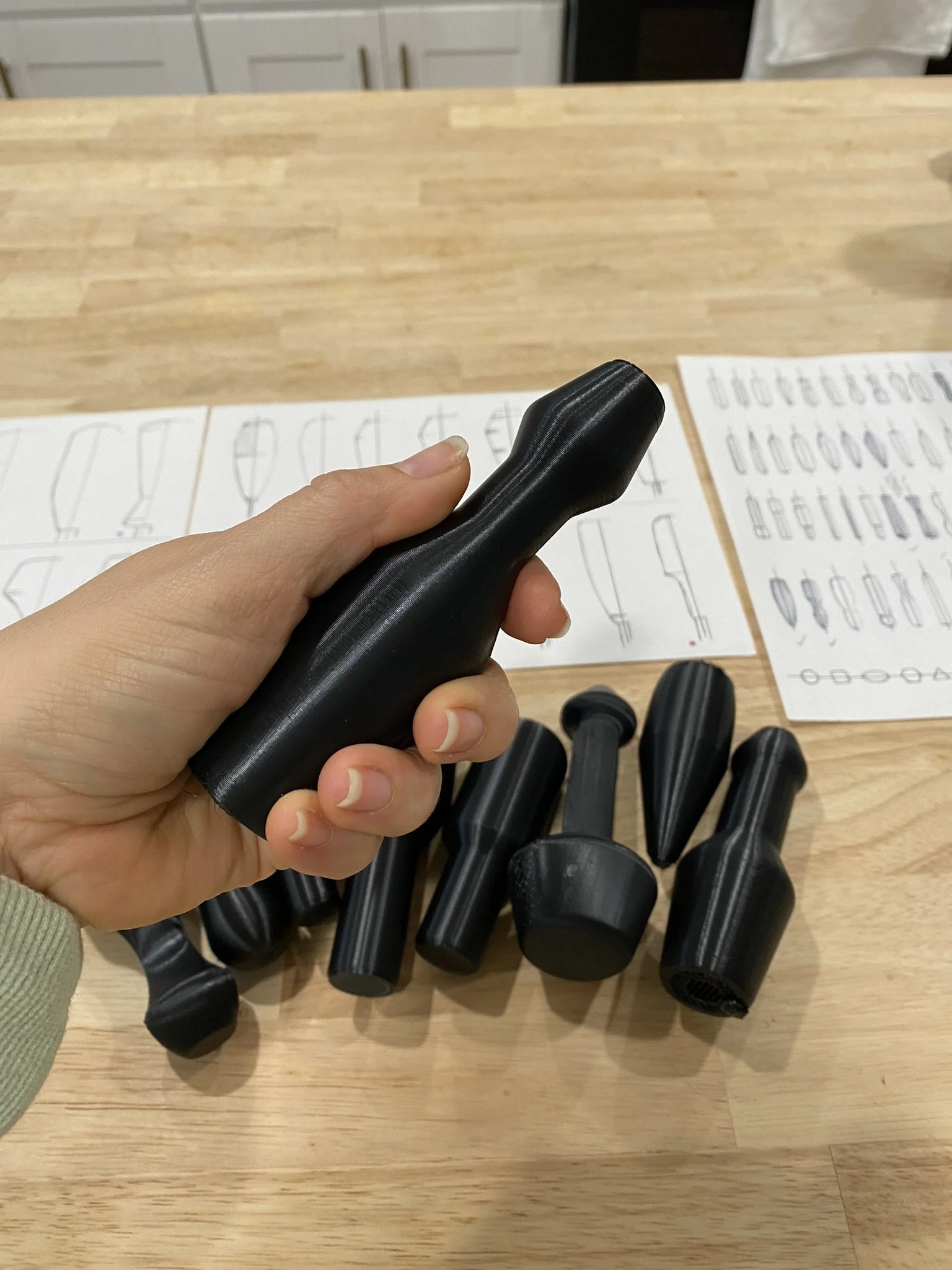 A hand holding a black golf club grip with multiple golf clubs laid out on a wooden surface and instruction sheets in the background.