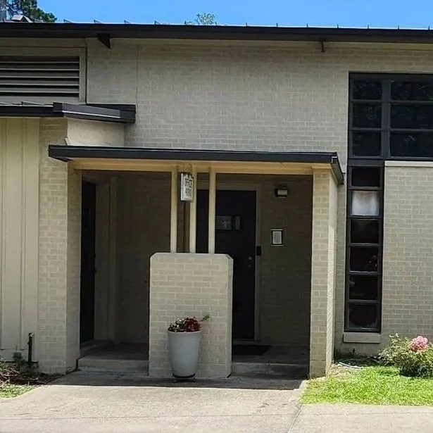 Front entrance of a modern house with a small porch, potted plant, brick pillars, and large window panels.
