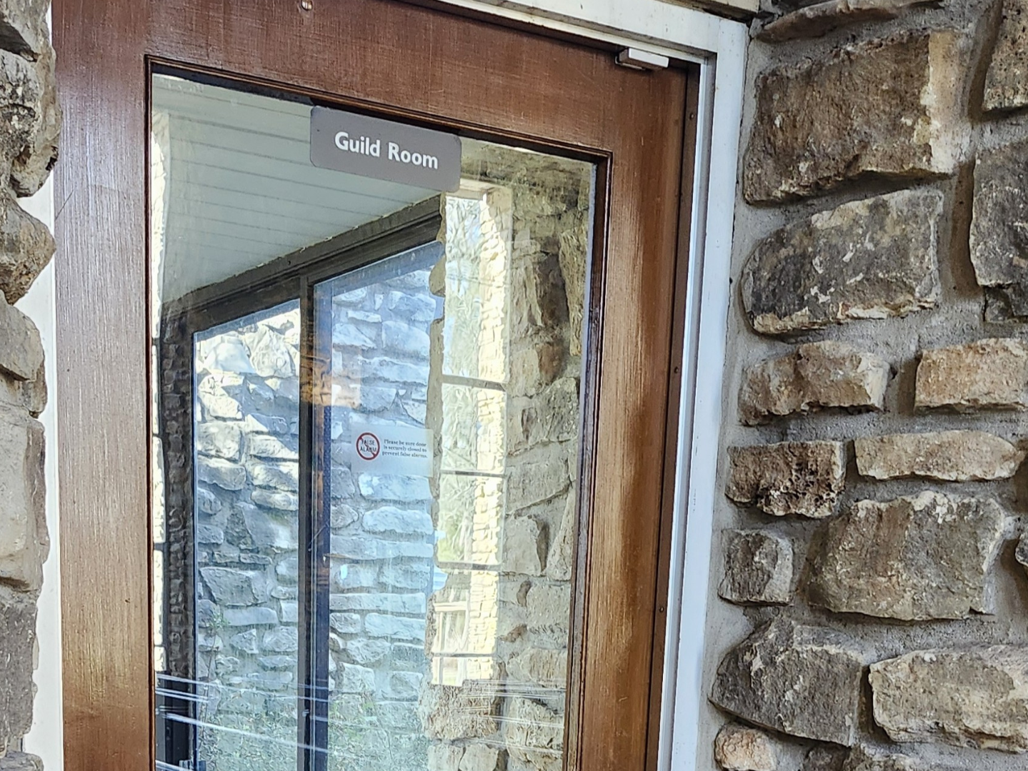 Wooden door with a glass window and a 'Guild Room' sign, surrounded by stone brick walls.