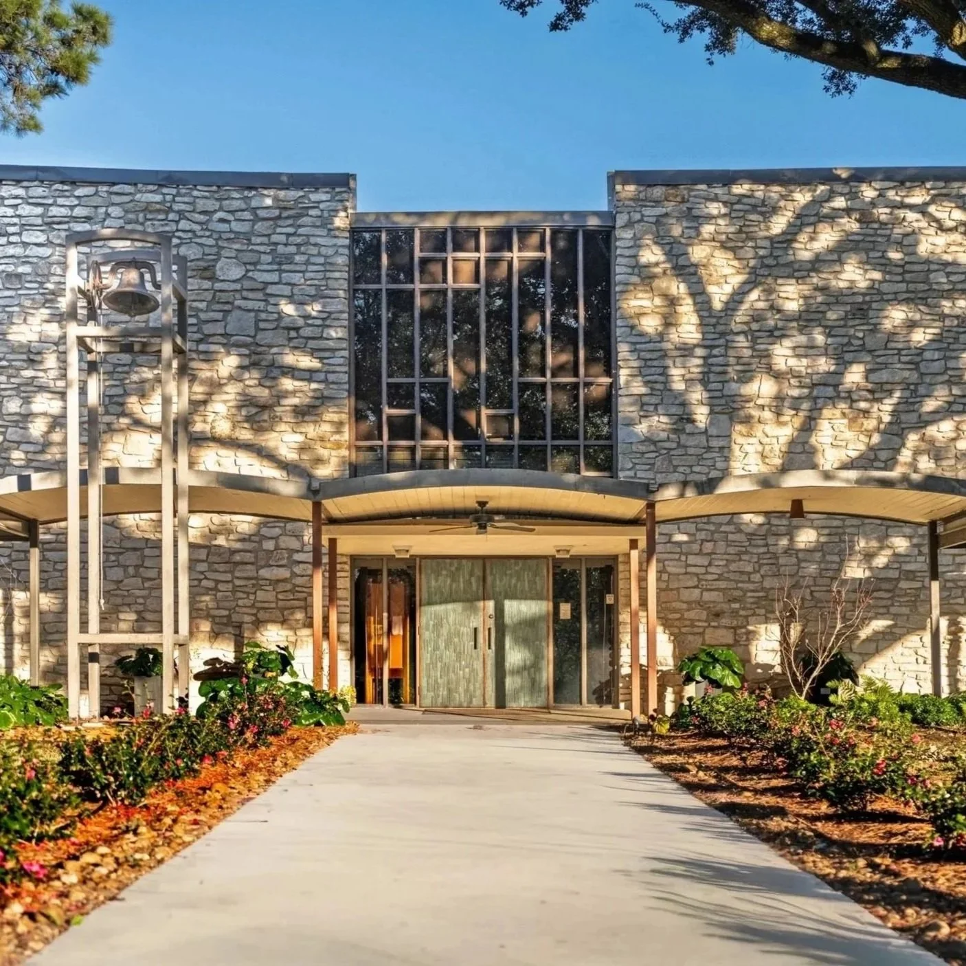 The exterior front entrance of St. Stephen's Episcopal Church in Beaumont, Texas, featuring a beautiful stone facade, a paved walkway, and landscaped gardens under a clear blue sky.
