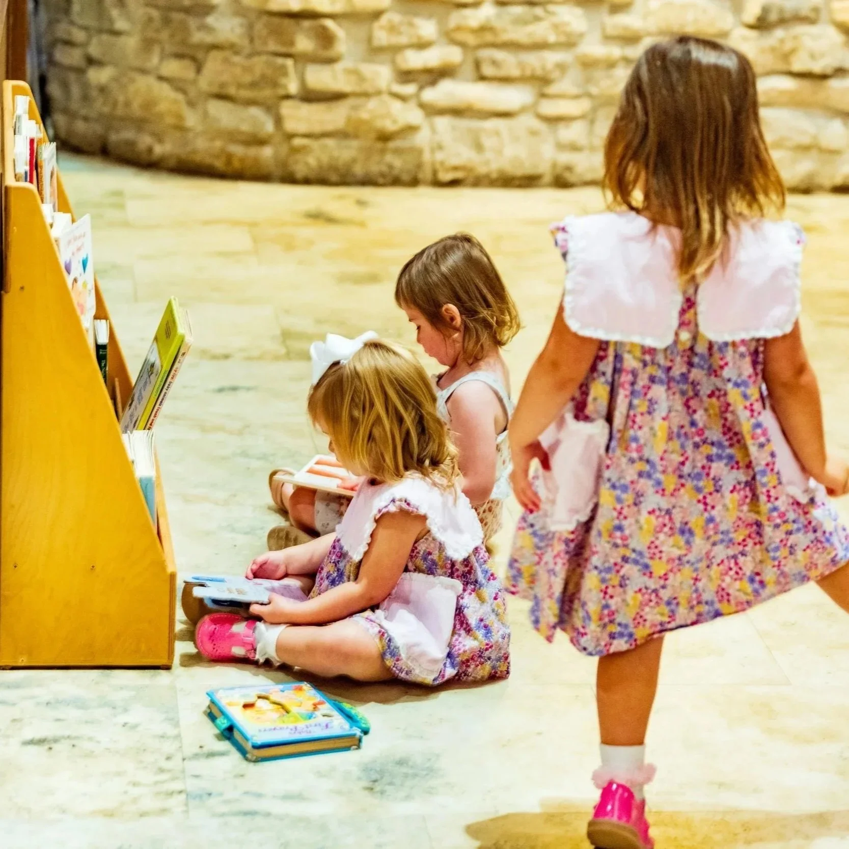 Three young children wearing flowered dresses with peplum collars while sitting in the back of the church and reading books at a St. Stephen's Episcopal Church service.