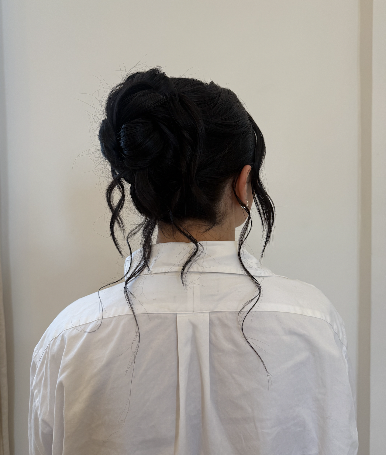 Woman with dark hair in an elegant updo, seen from behind, wearing a white shirt with a pleat in the back.