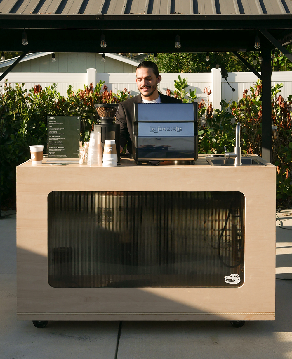 young barista in front of a coffee cart with menu, espresso machine and cups