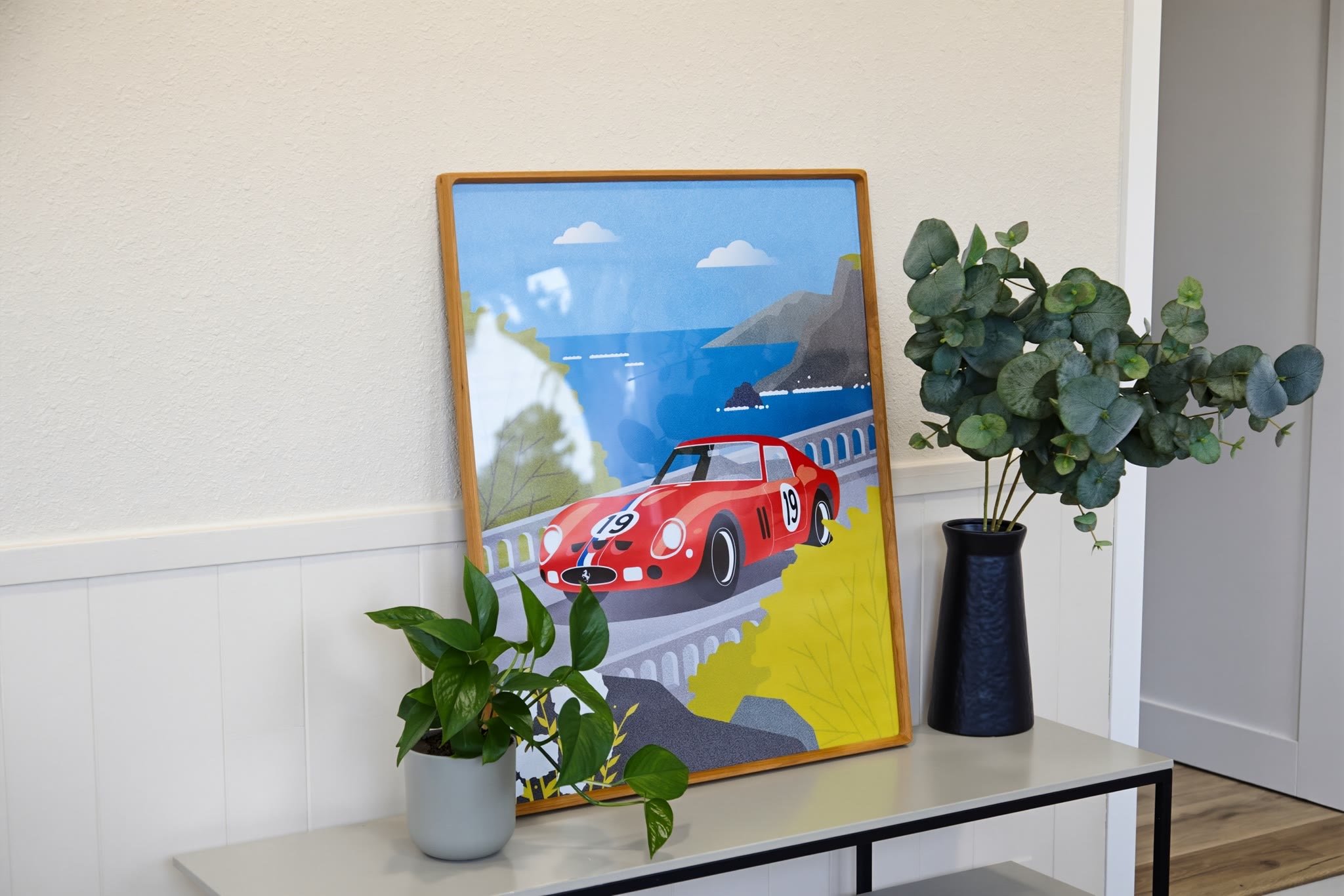 Framed poster featuring a red race car with the number 19, set against a scenic coastal background with cliffs, ocean, and blue sky.