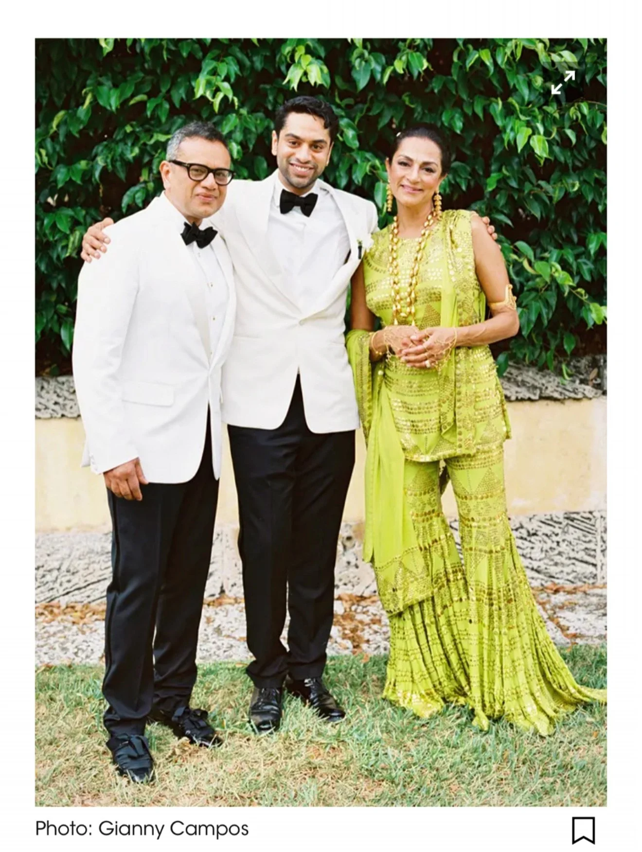 Three people dressed in formal attire, standing outdoors in front of a leafy green background.