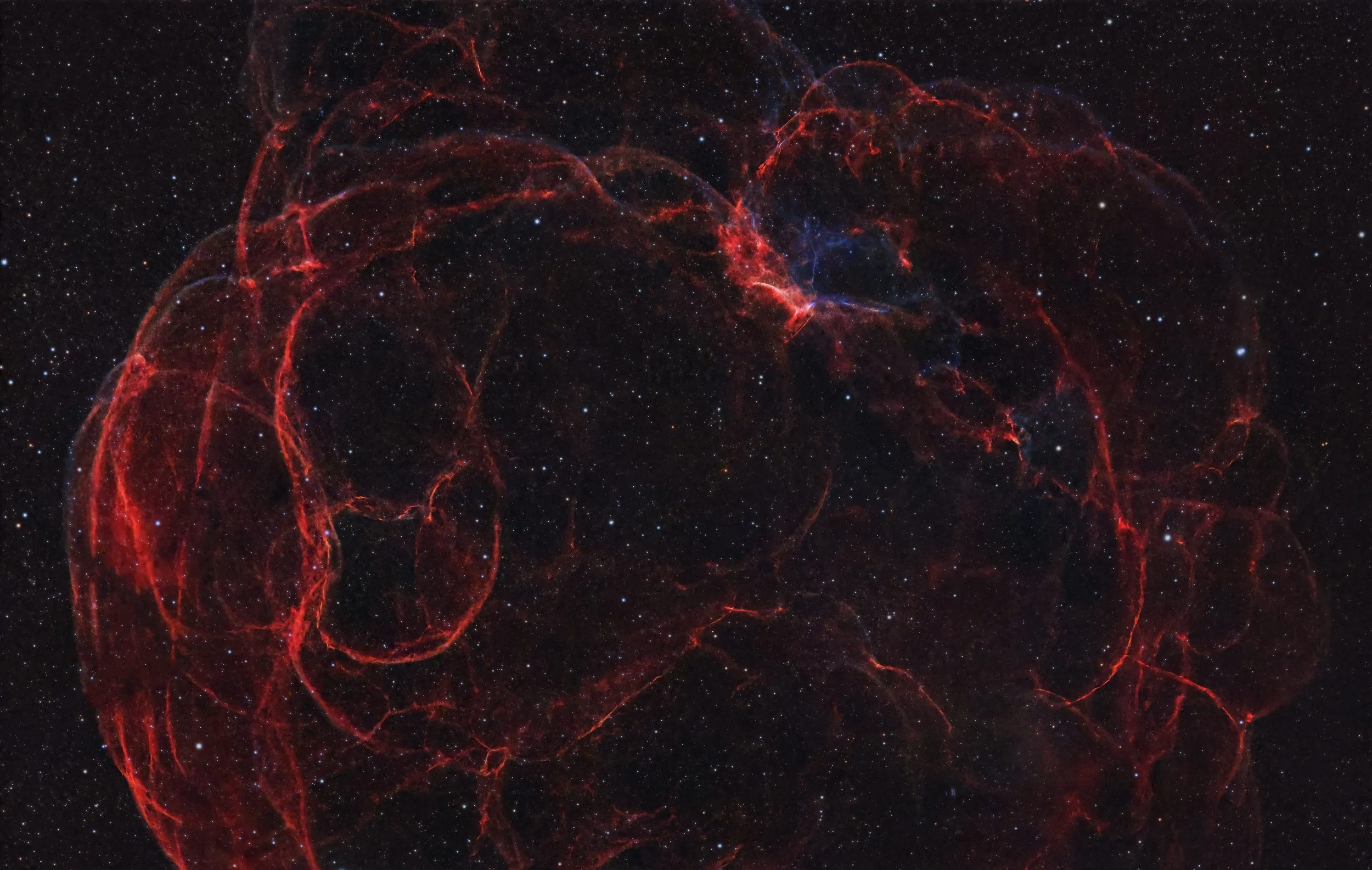A deep space image of a nebula with red gaseous filaments and a background filled with numerous small stars.