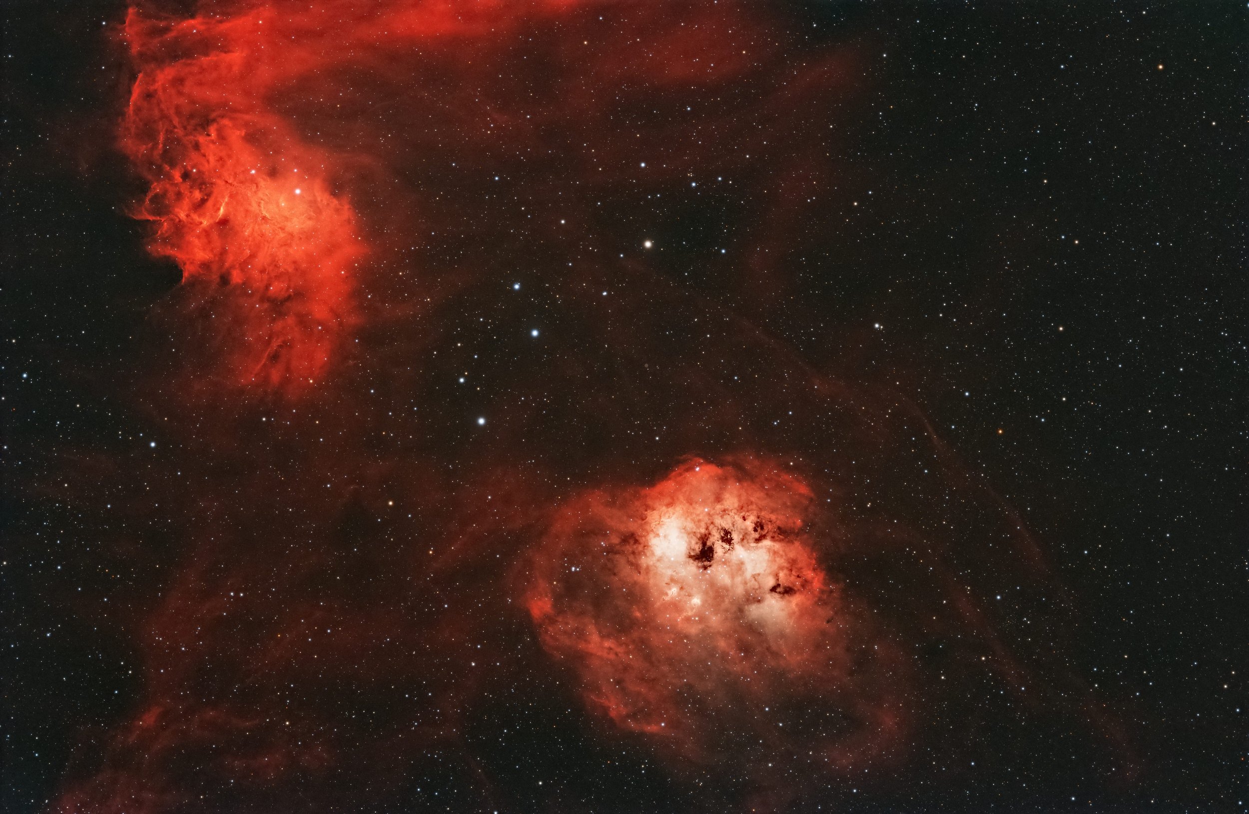 A stunning view of space showing two bright, orange-red nebulae surrounded by numerous stars and cosmic dust.