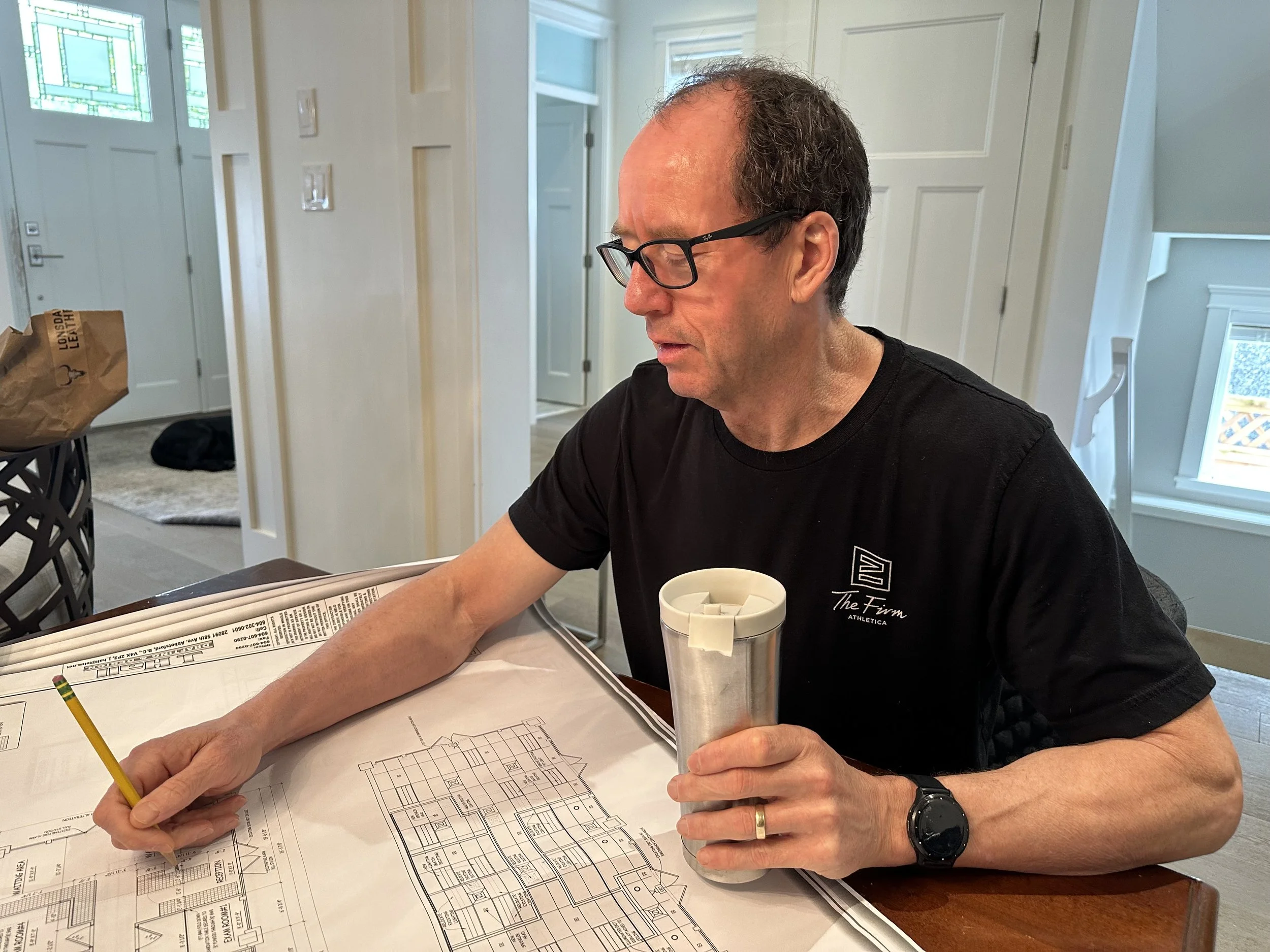Dr. Art Ceballos is sitting at a table and working on the Bayview Animal Hospital architectural blueprints, and reviewing the space for clinic needs.