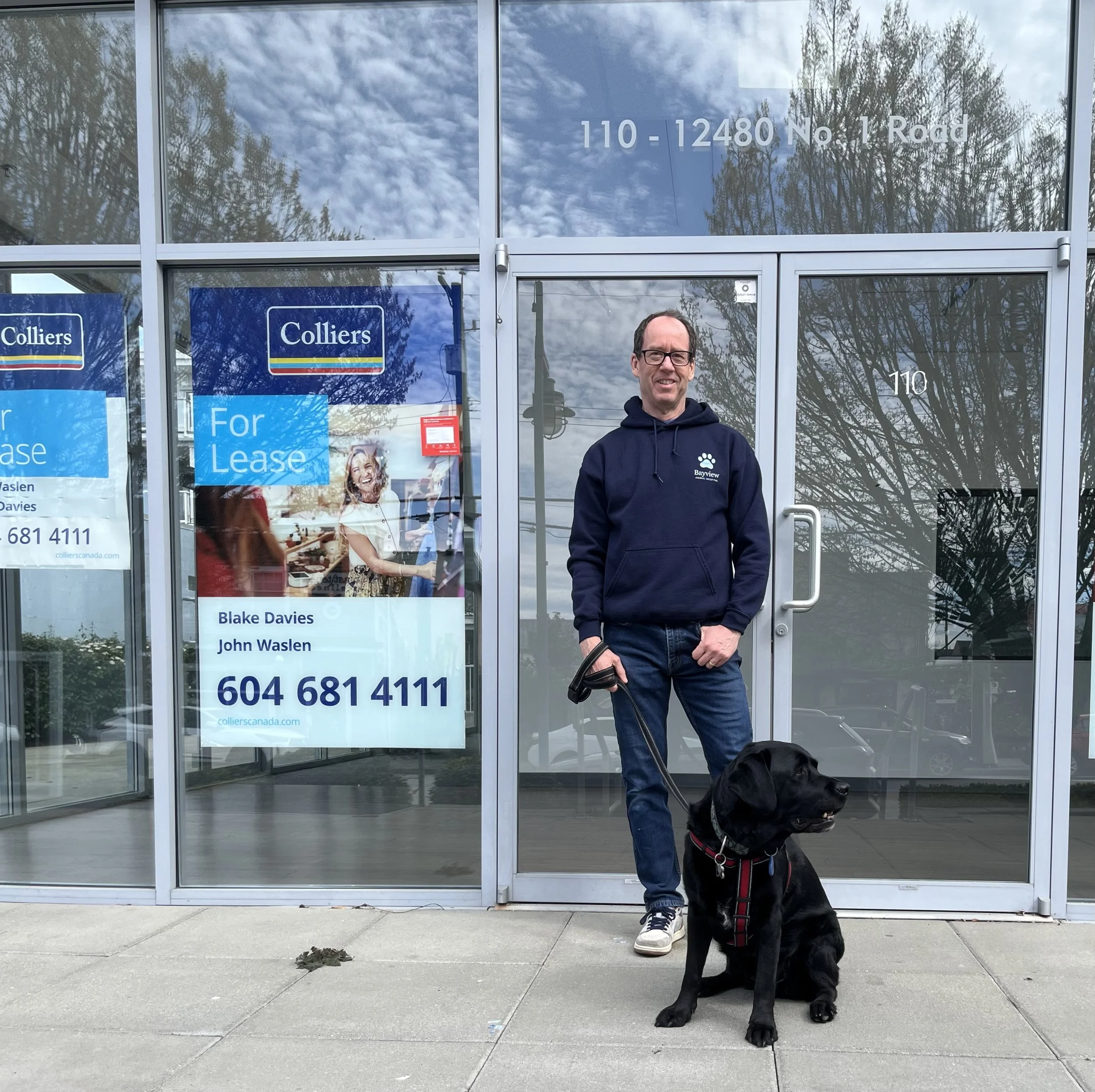 Dr. Art Ceballos standing outside of the new Bayview Animal Hospital site with his black lab. The new clinic opens Fall 2026.