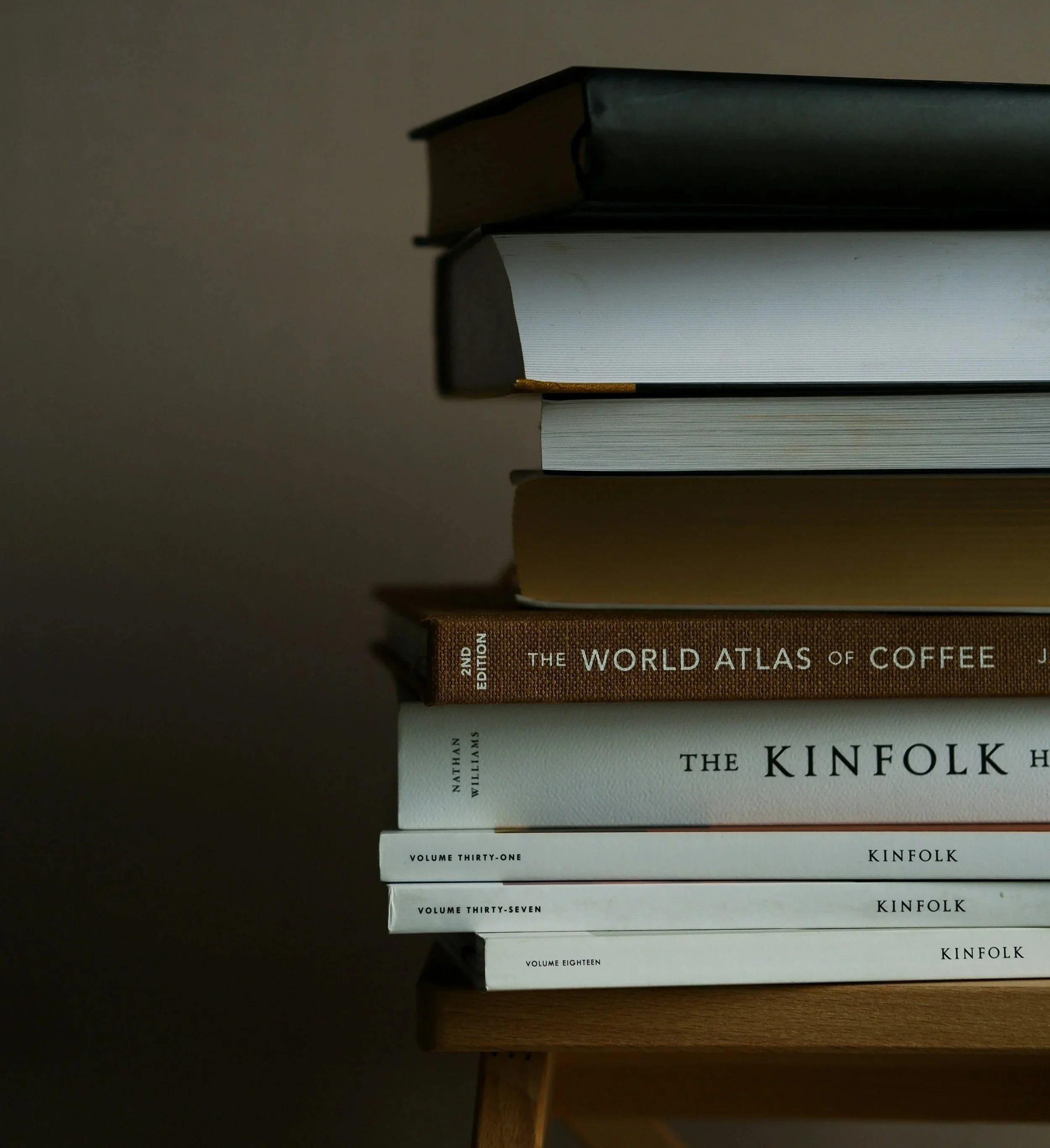 Stacked books on a wooden surface, including titles like 'The World Atlas of Coffee' and 'The Kinfolk Home'.