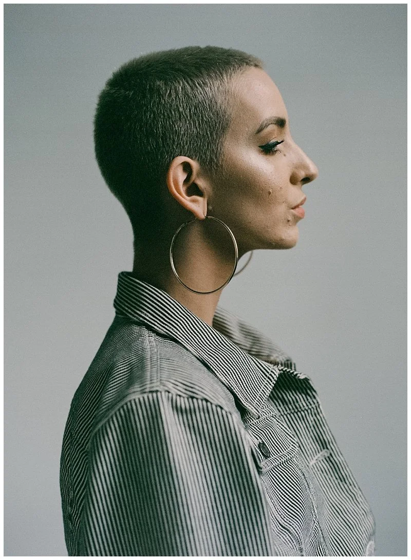 Profile of a woman with a buzz cut hairstyle, large hoop earrings, and a striped button-up shirt against a plain background.