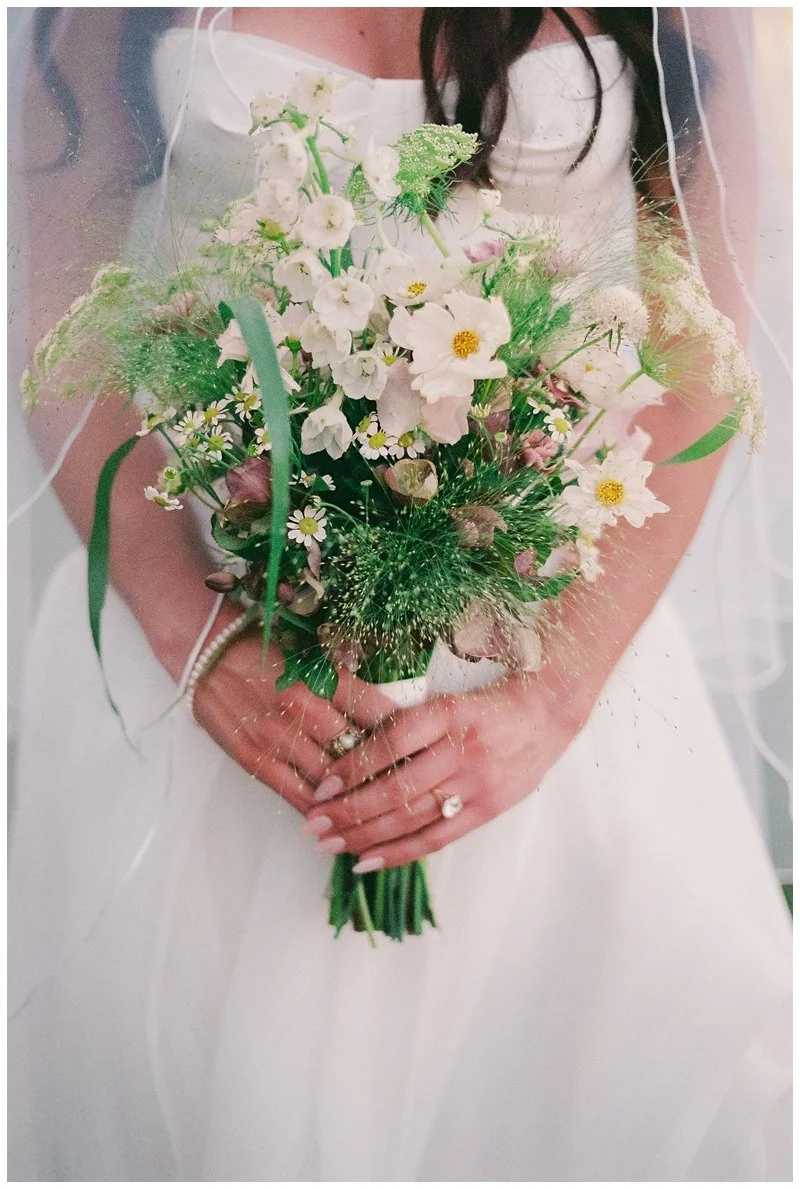 A bride holding a bouquet of mixed white and pink flowers with greenery.