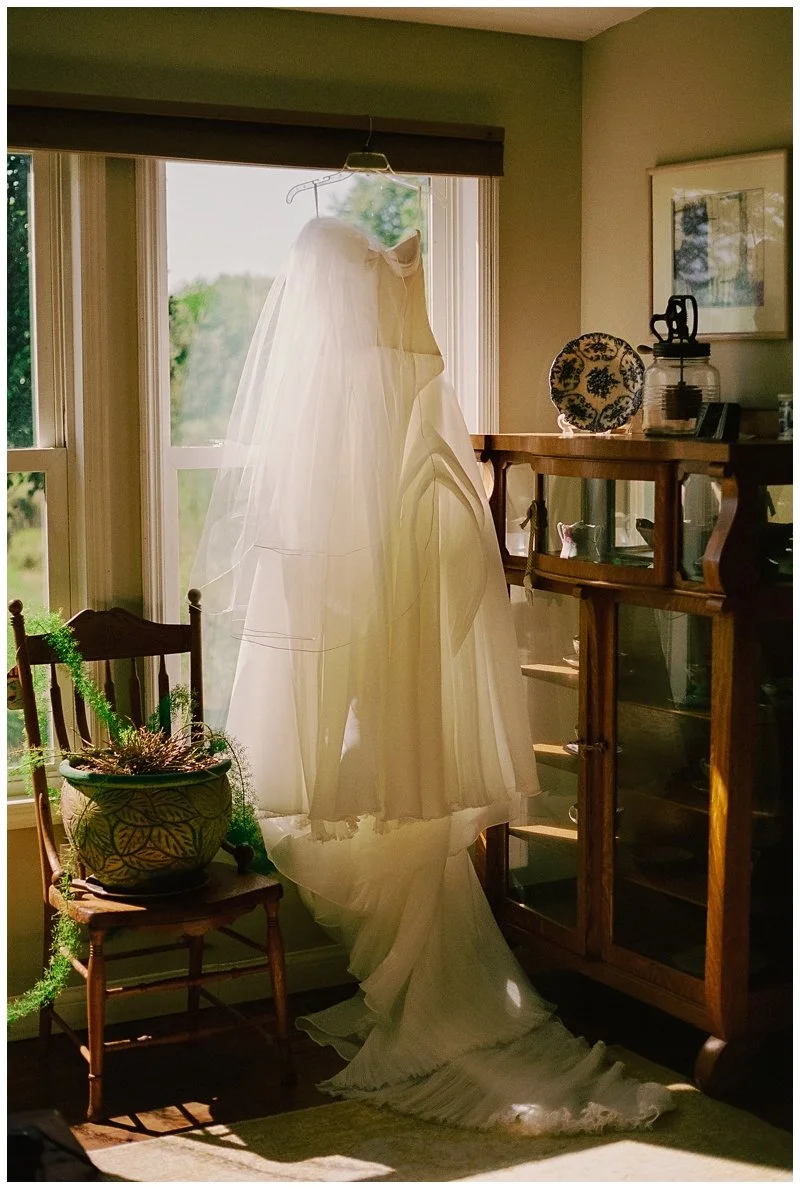 A wedding dress hanging near a window in a cozy, well-lit room.