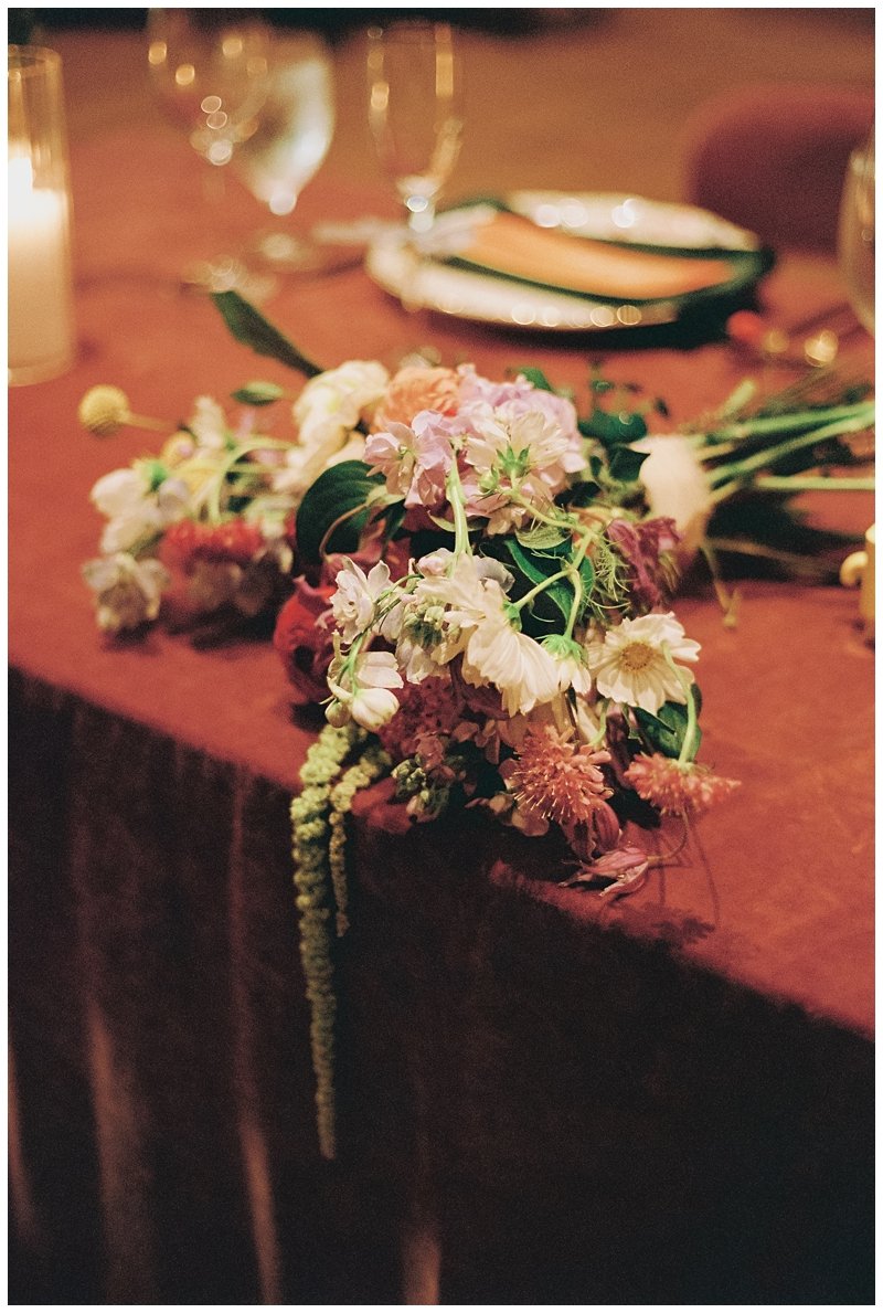 A bouquet of various pink and white flowers on a table with wine glasses and plates.