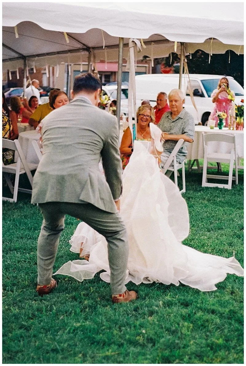 A bride and groom dancing at an outdoor wedding reception under a white tent, with guests seated at tables around them.