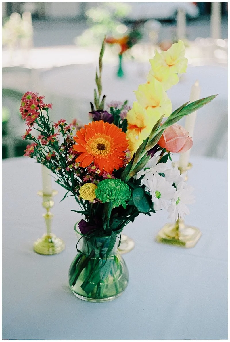 Colorful bouquet of mixed flowers in a small glass vase on a white table.
