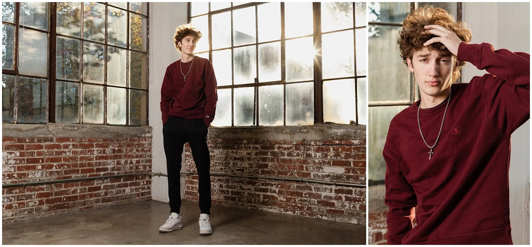 A young man with curly hair stands in a brick-walled industrial space with large windows, wearing a maroon sweatshirt, black pants, white sneakers, and a cross necklace. In a close-up, he touches his curly hair with a serious expression. Senior shoot