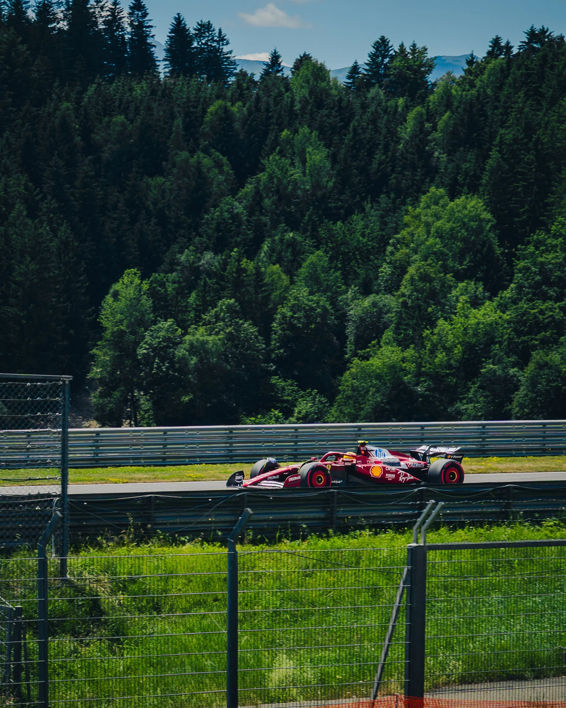 Ein rotes Formel-1-Auto auf einer Rennstrecke, umgeben von grünen Bäumen und Bergen im Hintergrund.