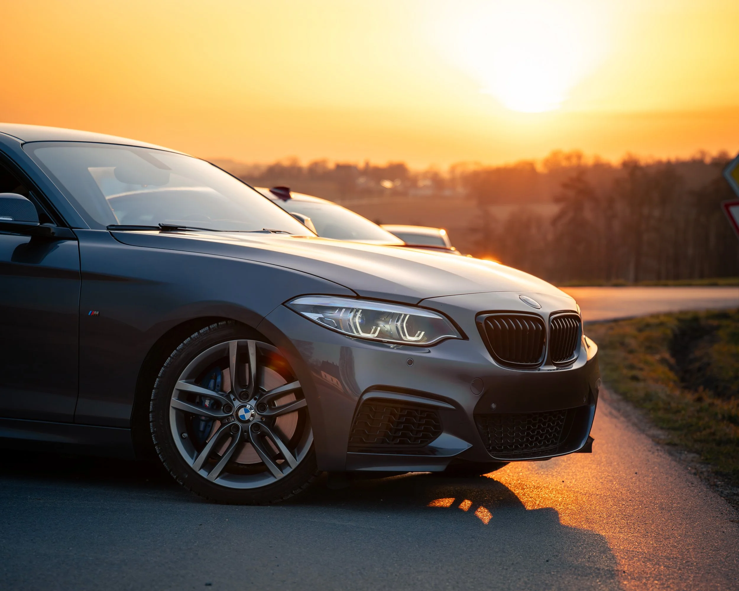 Ein grauer BMW M4 Sportwagen parkend bei Sonnenuntergang auf einer Landstraße.