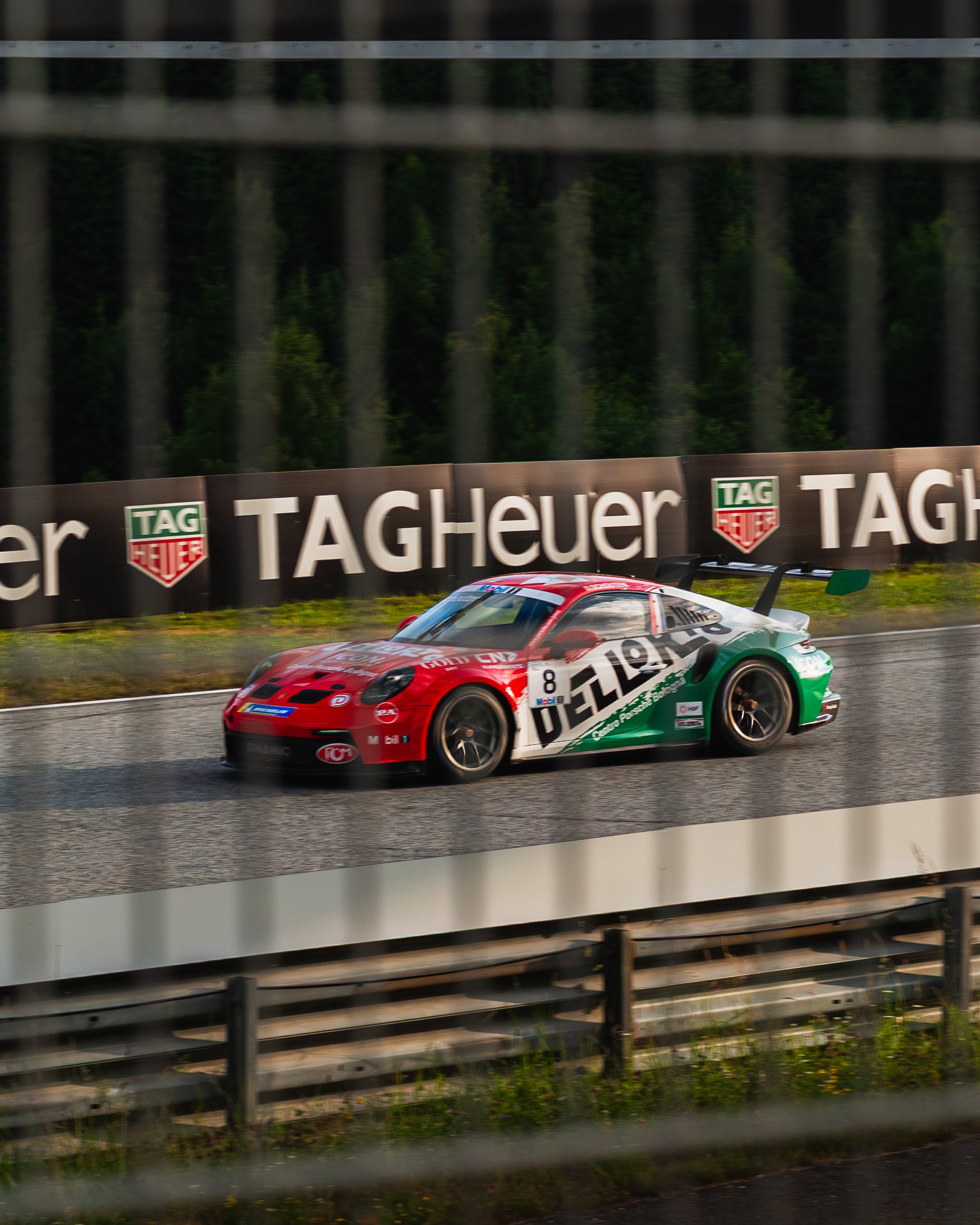 Ein Rennwagen auf einer Straße beim Rennen mit TAG Heuer Werbung im Hintergrund.