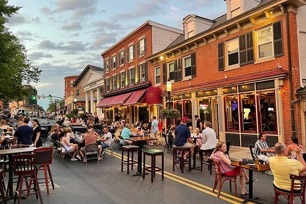 People dining outside at a restaurant on a busy city street during early evening.