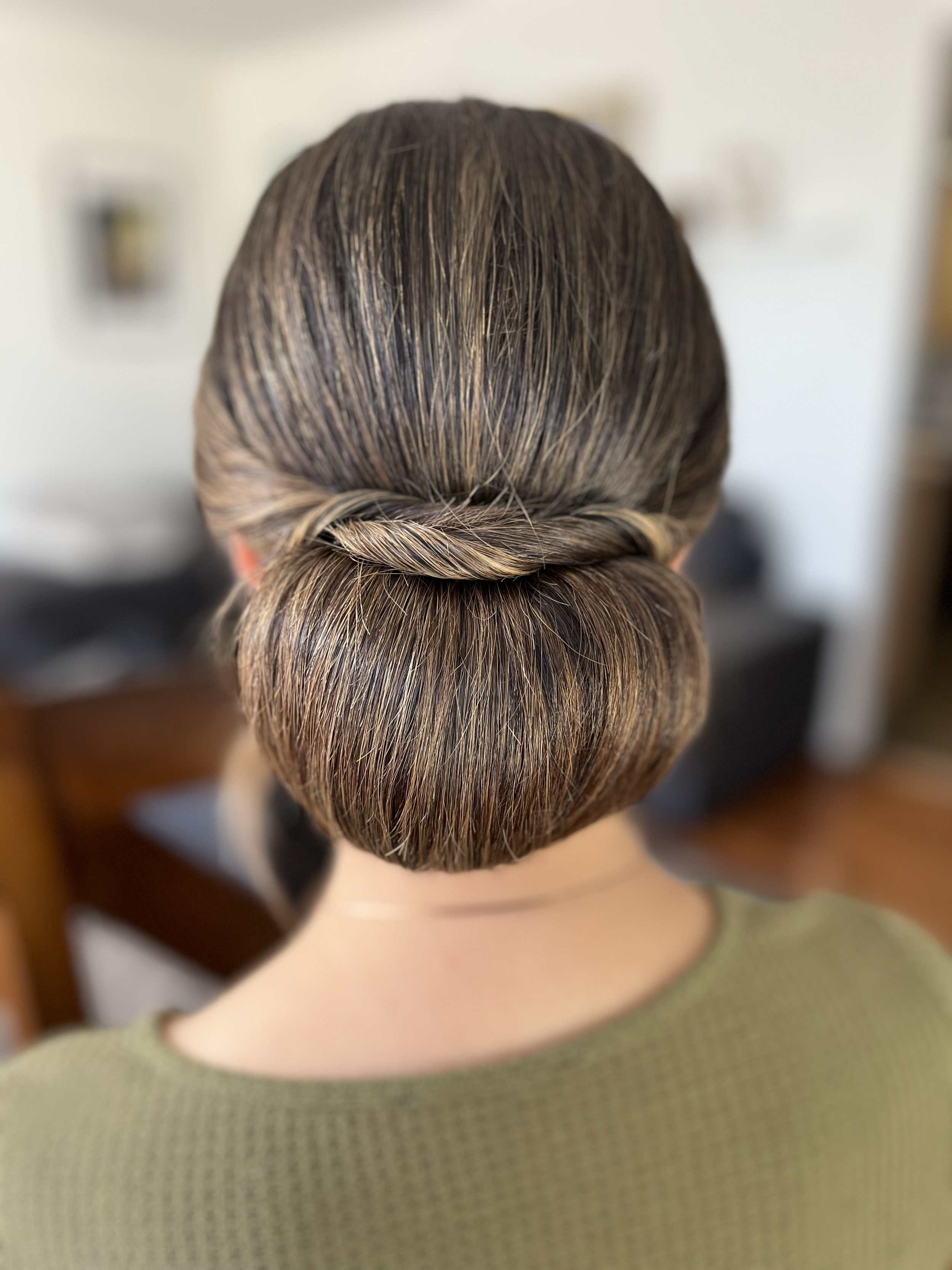 Back of a woman's head with a styled bun and a twisted hair detail, wearing an olive green top.