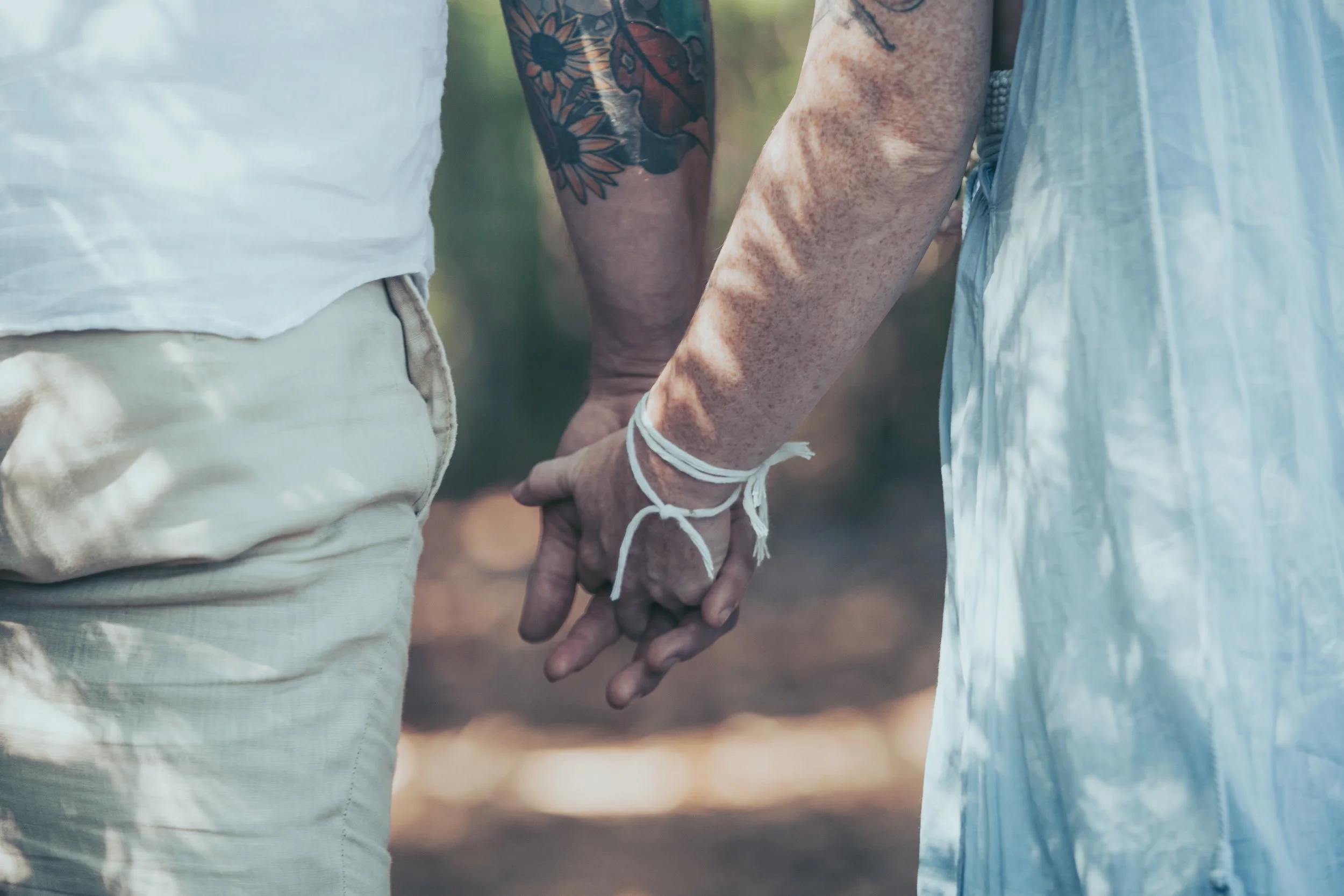 Close-up of two people holding hands, with one person's hand handcuffed with a white string. The individuals appear to be in an outdoor setting.