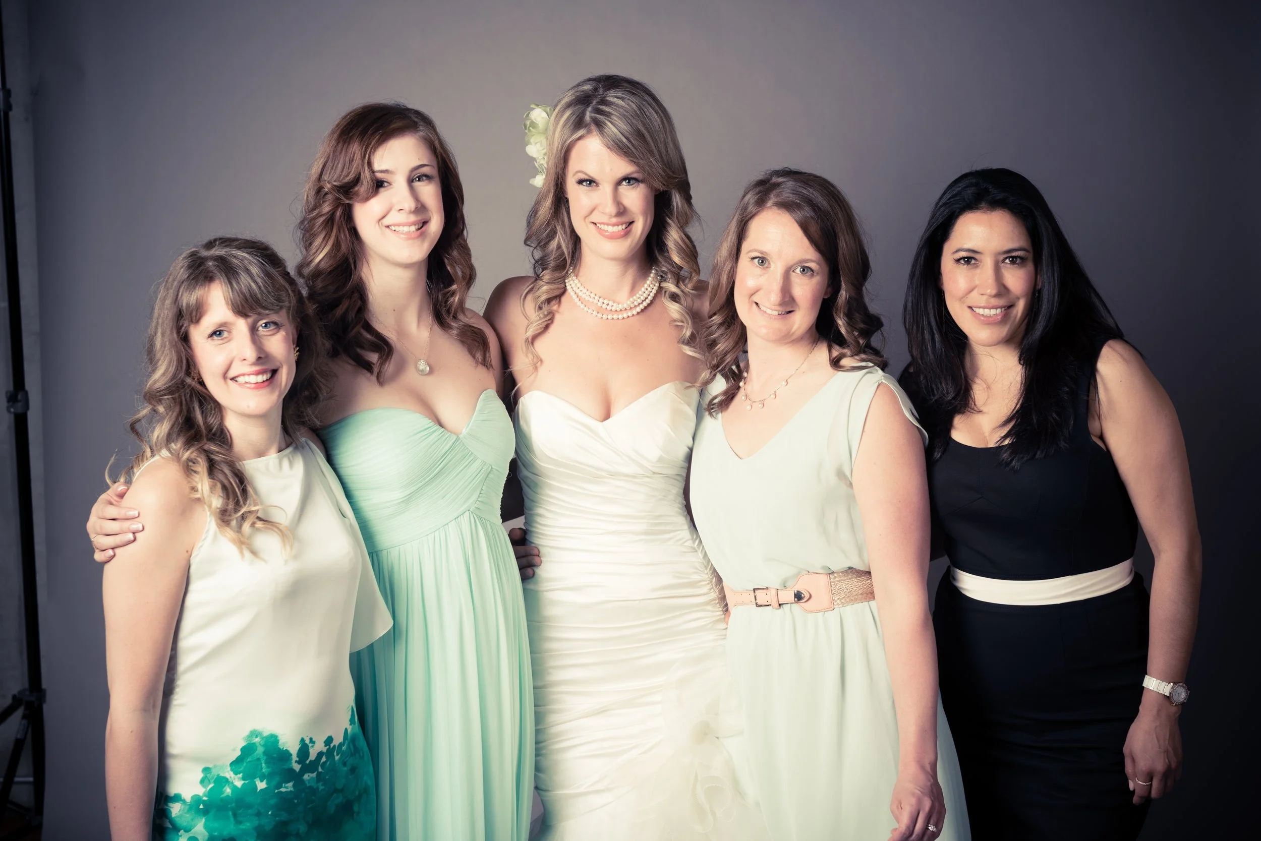 Five women in formal dresses posing together in a photo studio.