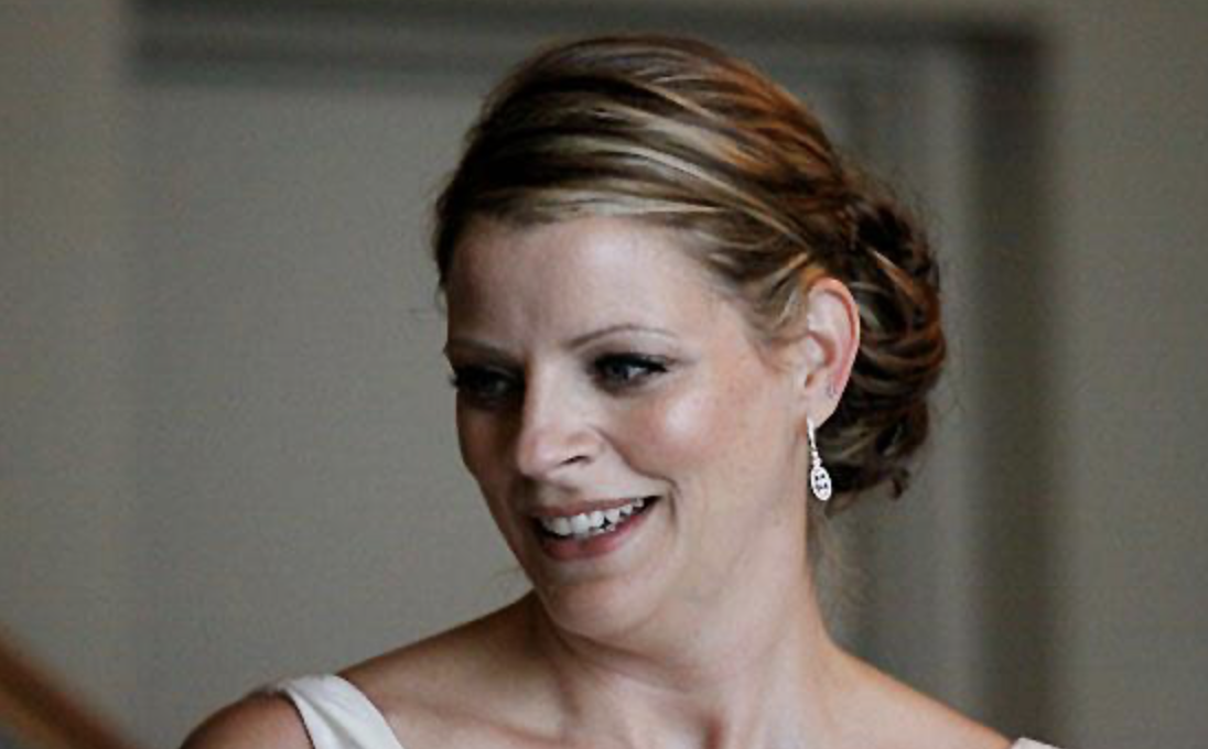 A woman with short, styled hair wearing earrings and a white dress.