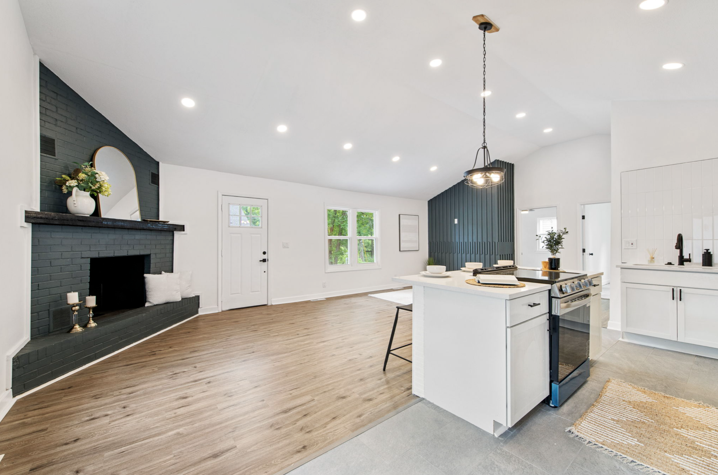 Open-concept living room and kitchen with hardwood and tile flooring, dark accent wall, fireplace with candles, and modern decor.